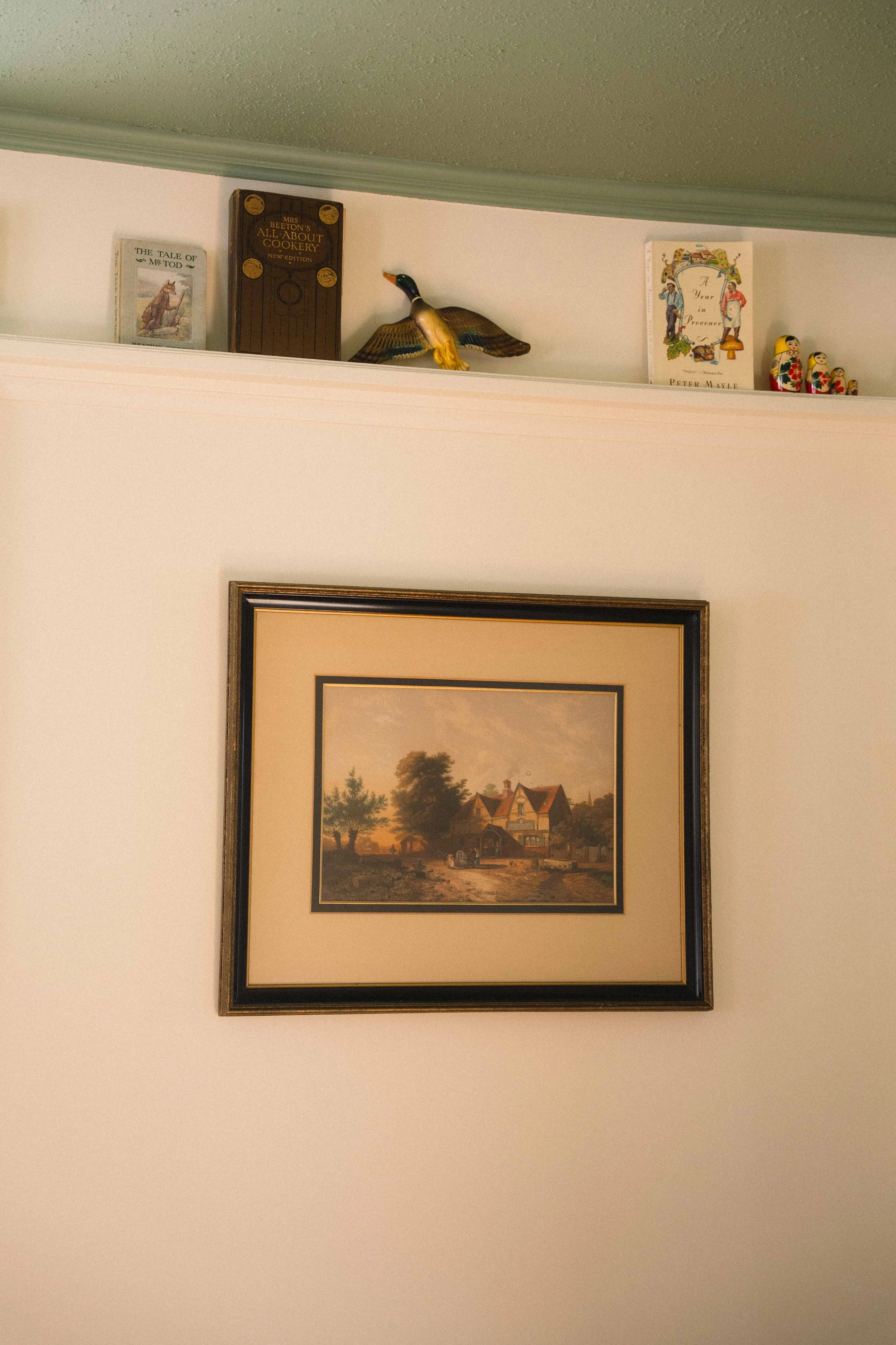 cottagecore framed wall art with picture rail featuring wooden duck, the tale of peter rabbit, and a year in provence with matryoshka dolls, and a green ceiling with cream walls