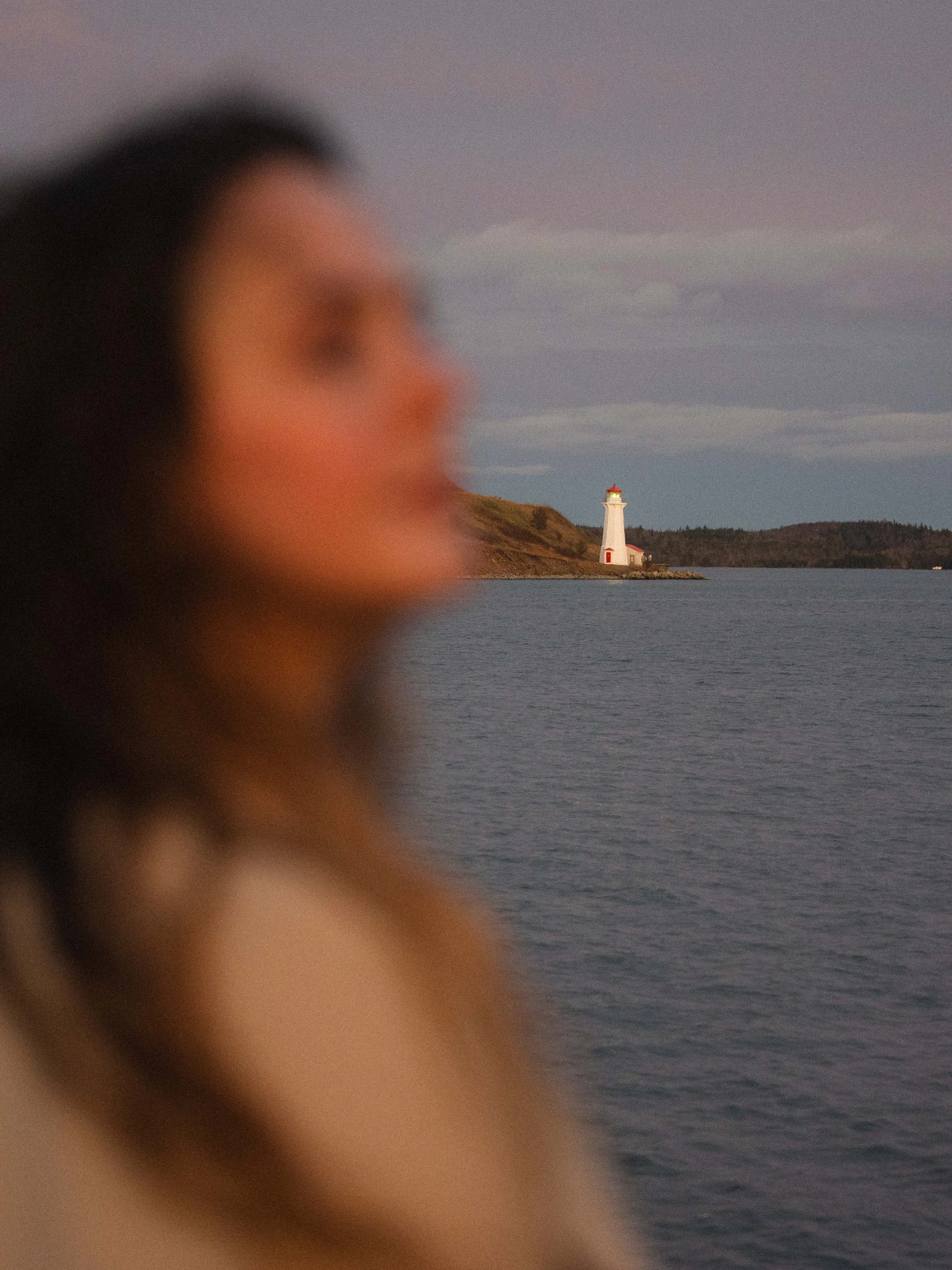 girl traveling to Halifax, Nova Scotia and looking out at sunset on the Waterfront at a lighthouse that is in focus while the silhouette of girl is blurred.
