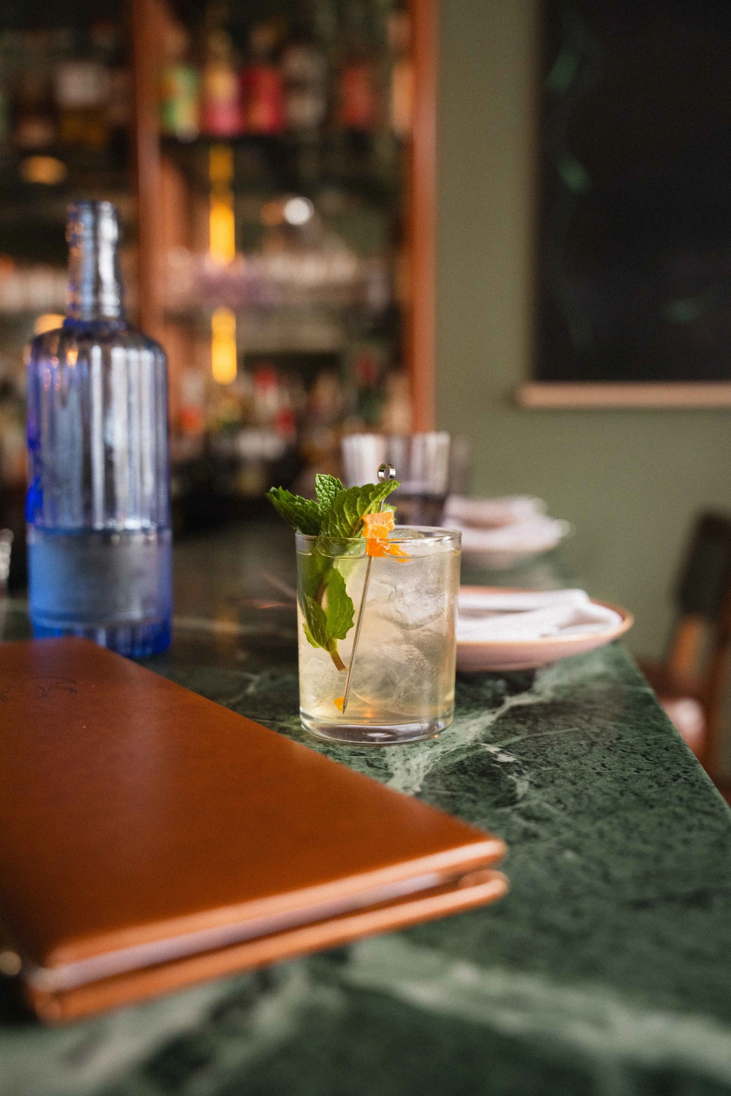 a cocktail glass on a stone countertop with a mint leaf as garnish with a art deco style bar blurred out in the background in one of Halifax's cocktail bars in a guide for travellers to the city