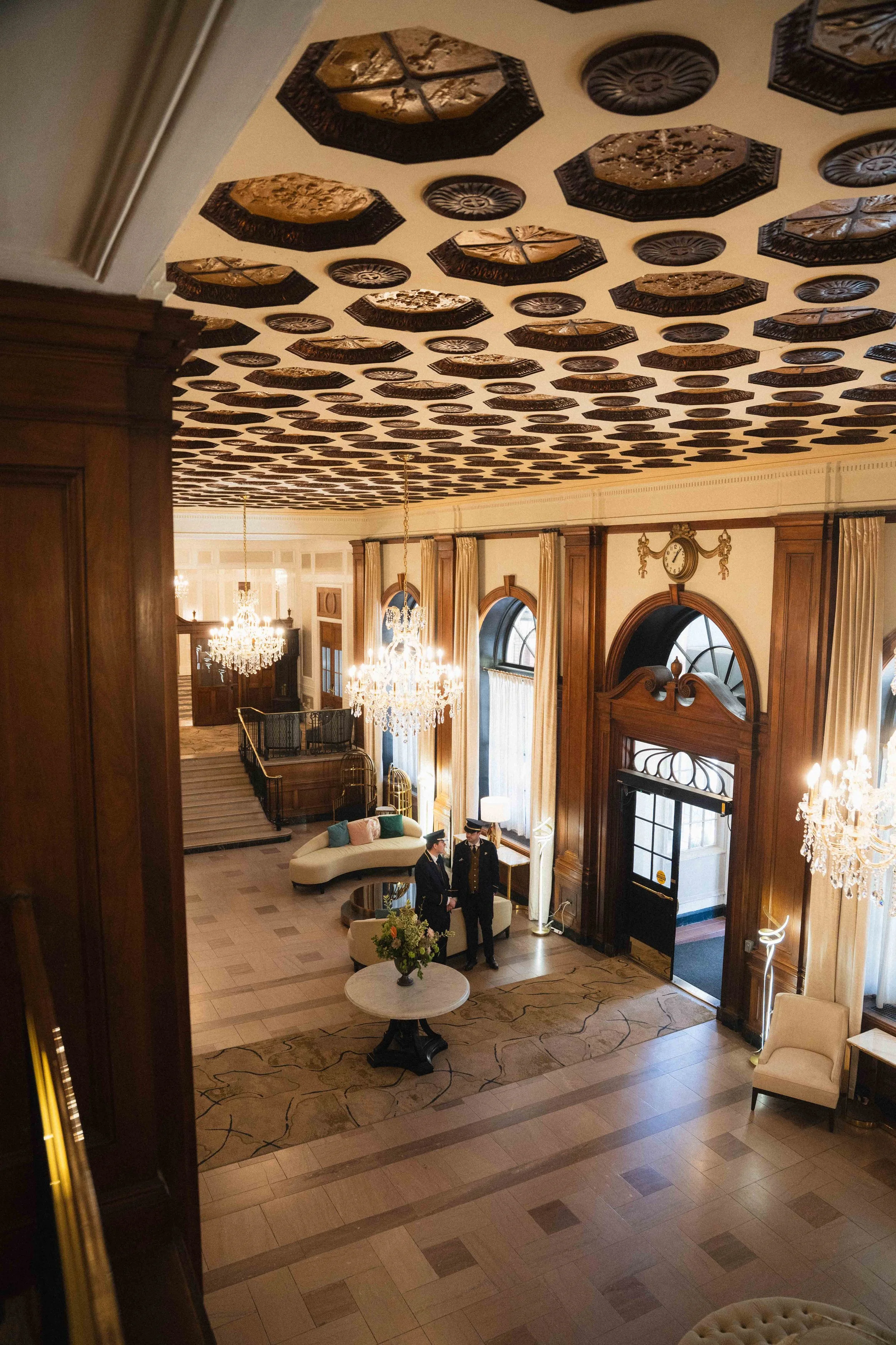 overlooking two bellhops conversing in an elegant hotel lobby. A historic railroad hotel Lord Nelson Inn & Suites in downtown Halifax next to Public Gardens