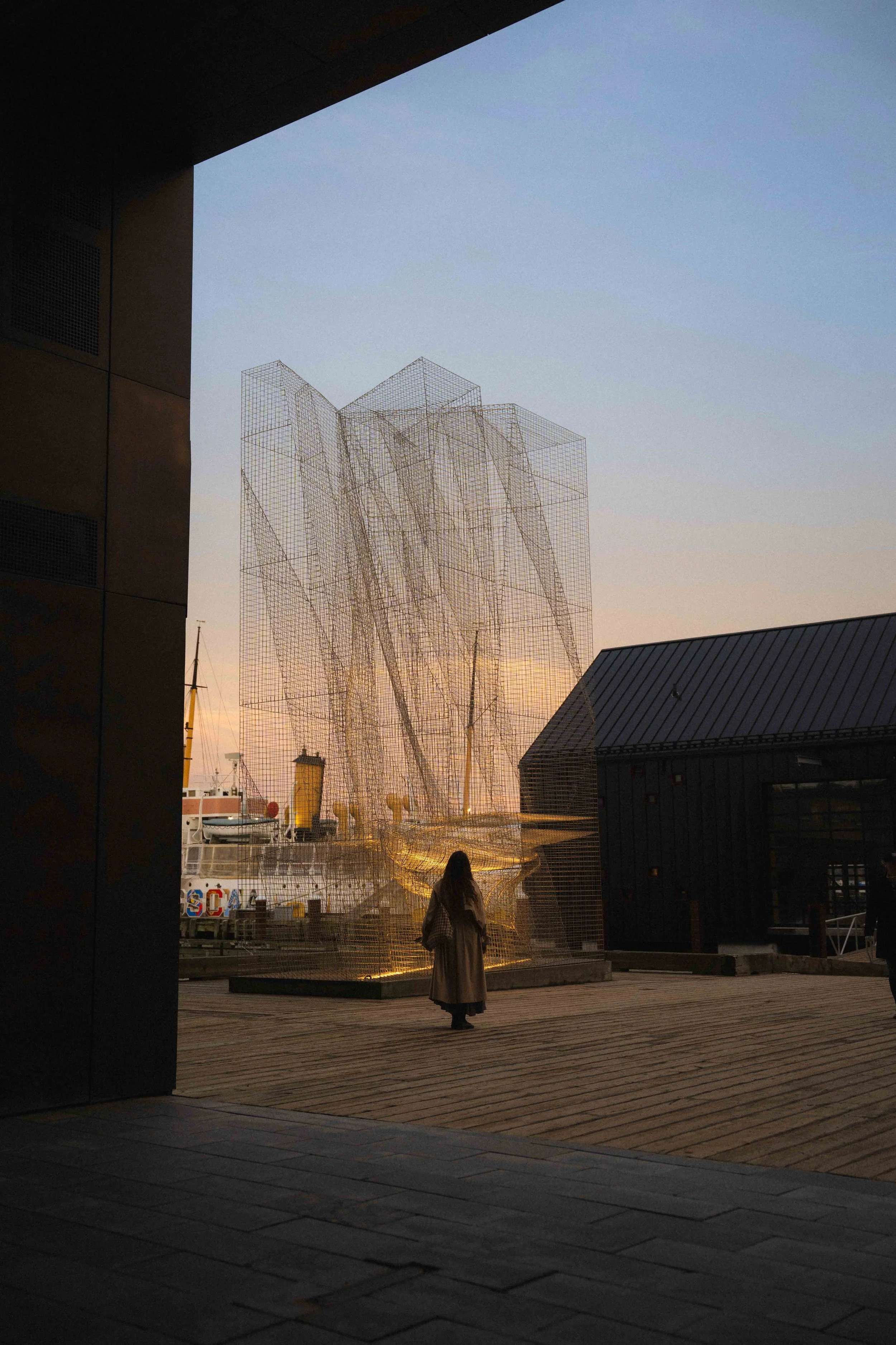 a girl standing looking up at the Halifax Waterfront modern art installation of a boat at blue hour, one of the best places to watch sunset when travelling to the city