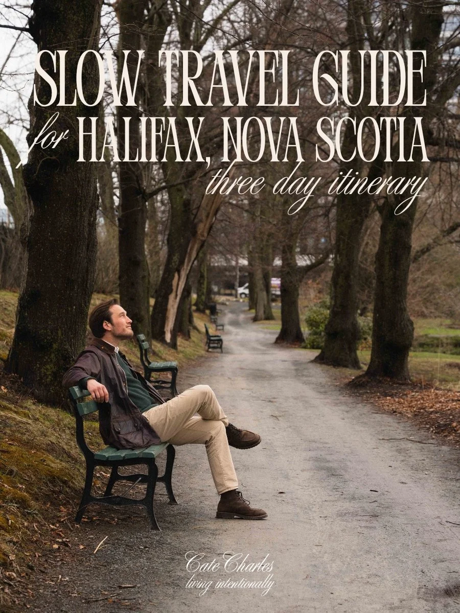 text reads Slow Travel Guide for Halifax, Nova Scotia three day itinerary, living intentionally. The image is of a man wearing dark academia style clothing sitting on a park bench along a path lined with large oak trees on a moody autumn day