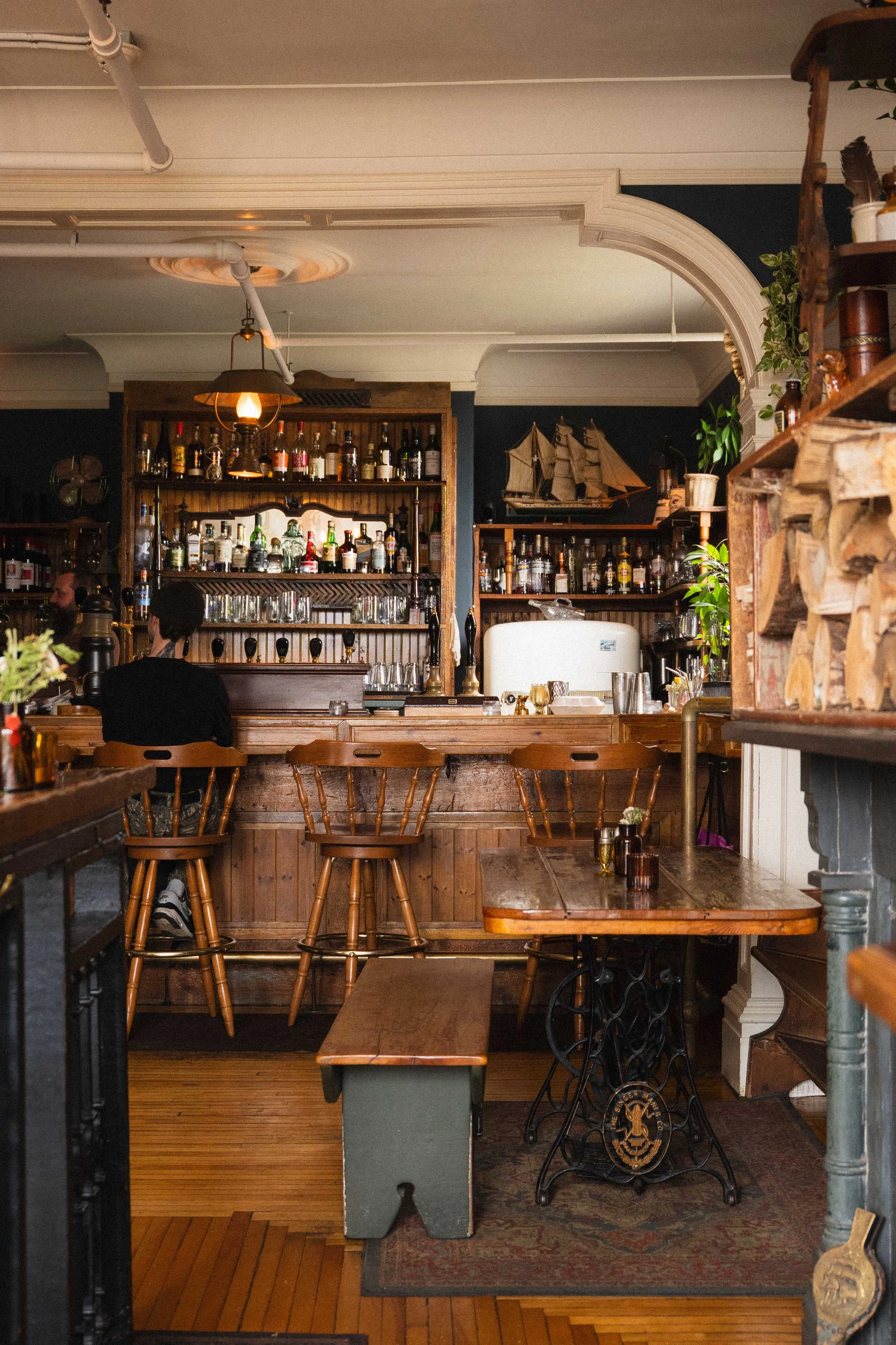 inside a historic pub called The Narrows in the North End of Halifax, Canada filled with antiques in a Victorian building. There is a schooner boat and a fireplace with wooden bar stools