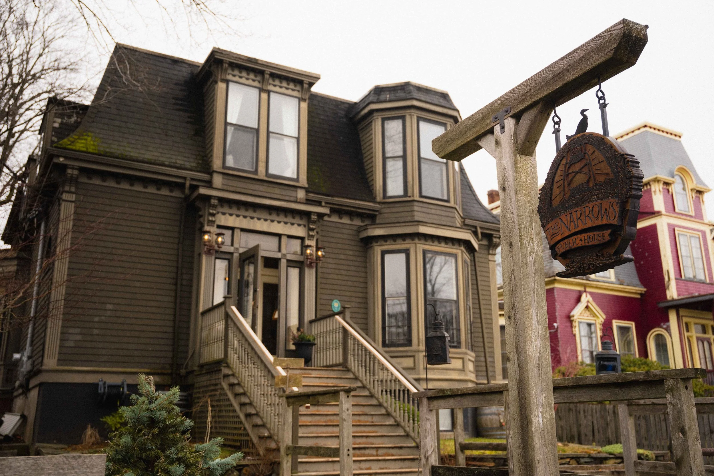 exterior shot of a victorian pub on a moody day in the city of Halifax Nova Scotia with a wooden sign post and carved sign that reads The Narrows Public House