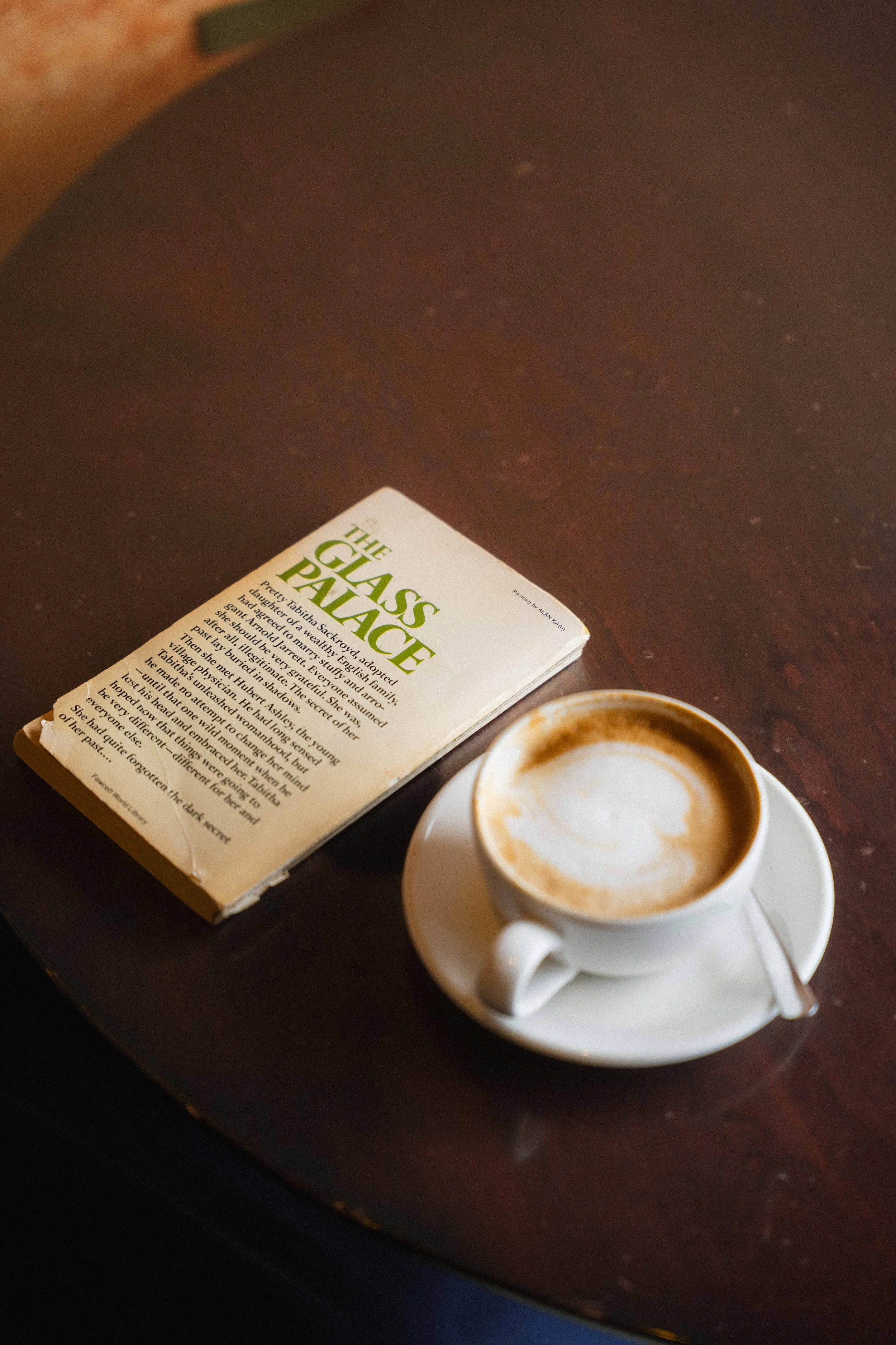 moody photography of an old book "The Glass Palace" and a cappuccino with heart latte art in a cozy bookstore in downtown Halifax, Canada