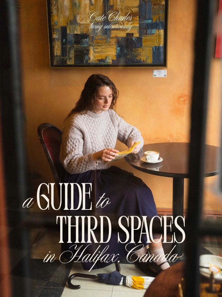 text reads a Guide to Third Spaces in Halifax, Canada, living intentionally. A girl is sitting in a cafe reading an old book and wearing a cozy vintage sweater and drinking a cappuccino through the window
