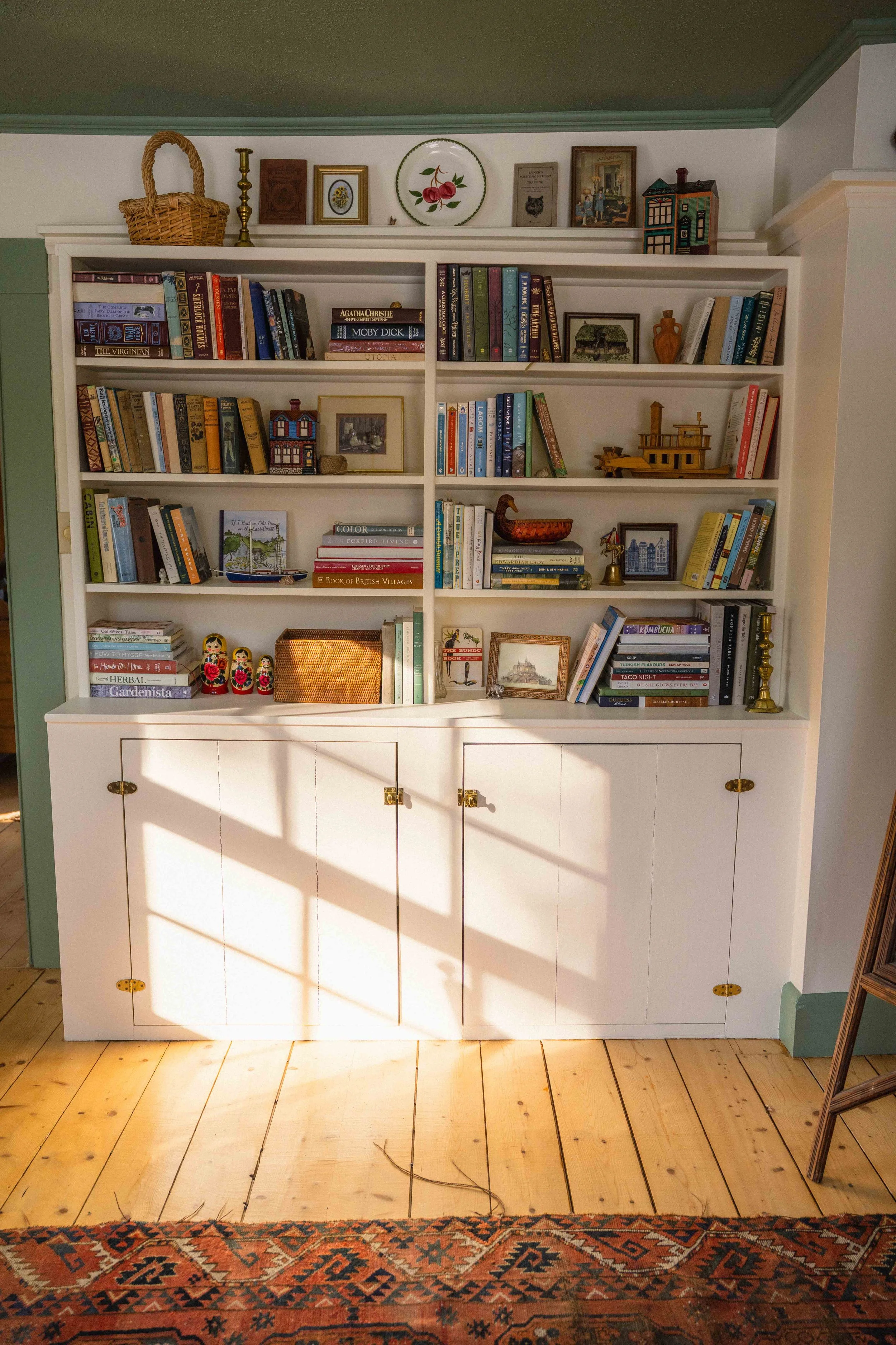 cream built-in bookshelves with colourful books and decor in a cottage style interior - green ceiling, red wool vintage rug, and brass hardware