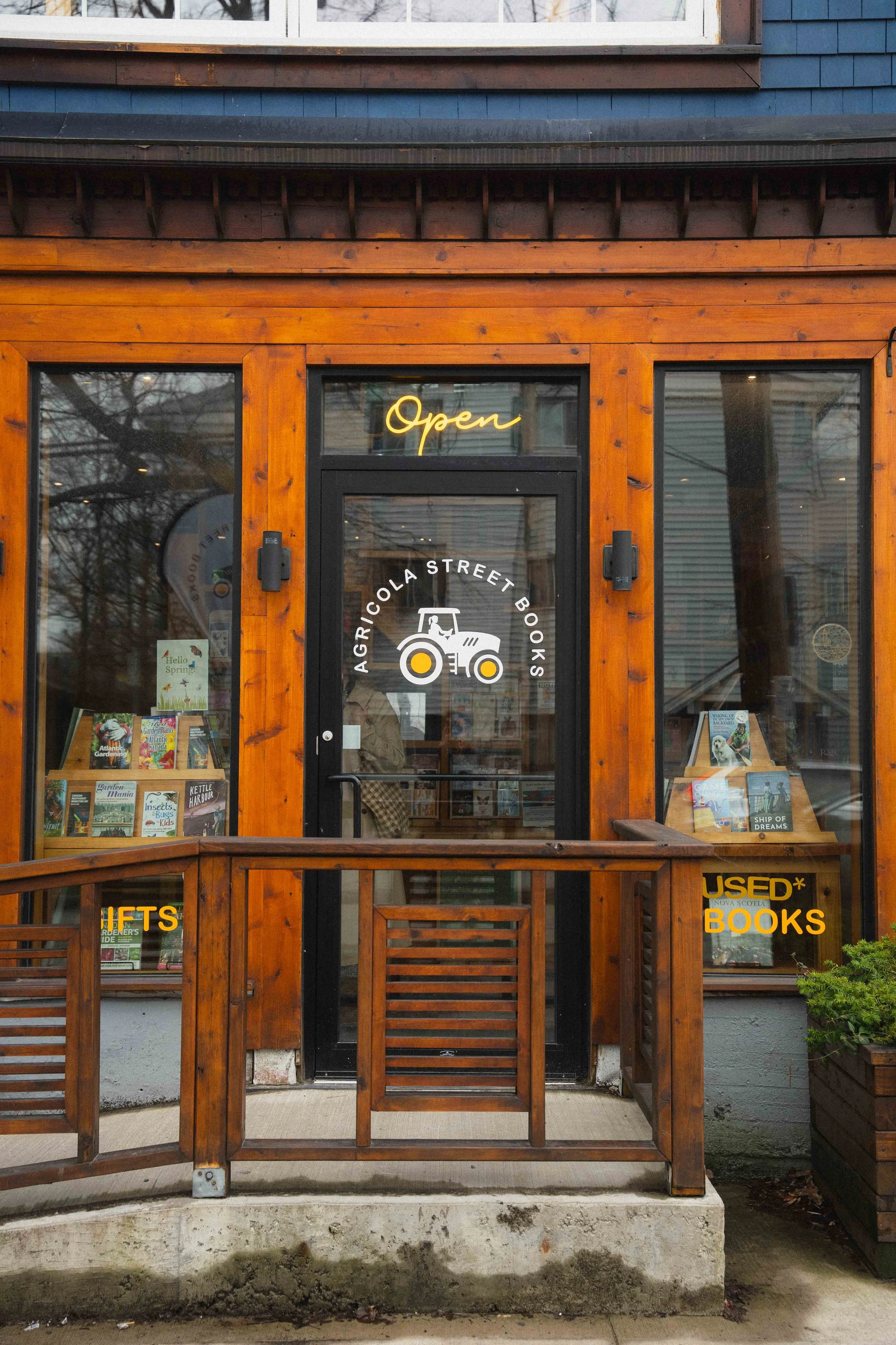 exterior of a wooden store with large wooden with an open sign and a tractor that reads agricola street books and used book and gifts in Halifax's North End in a guide to the city's third spaces