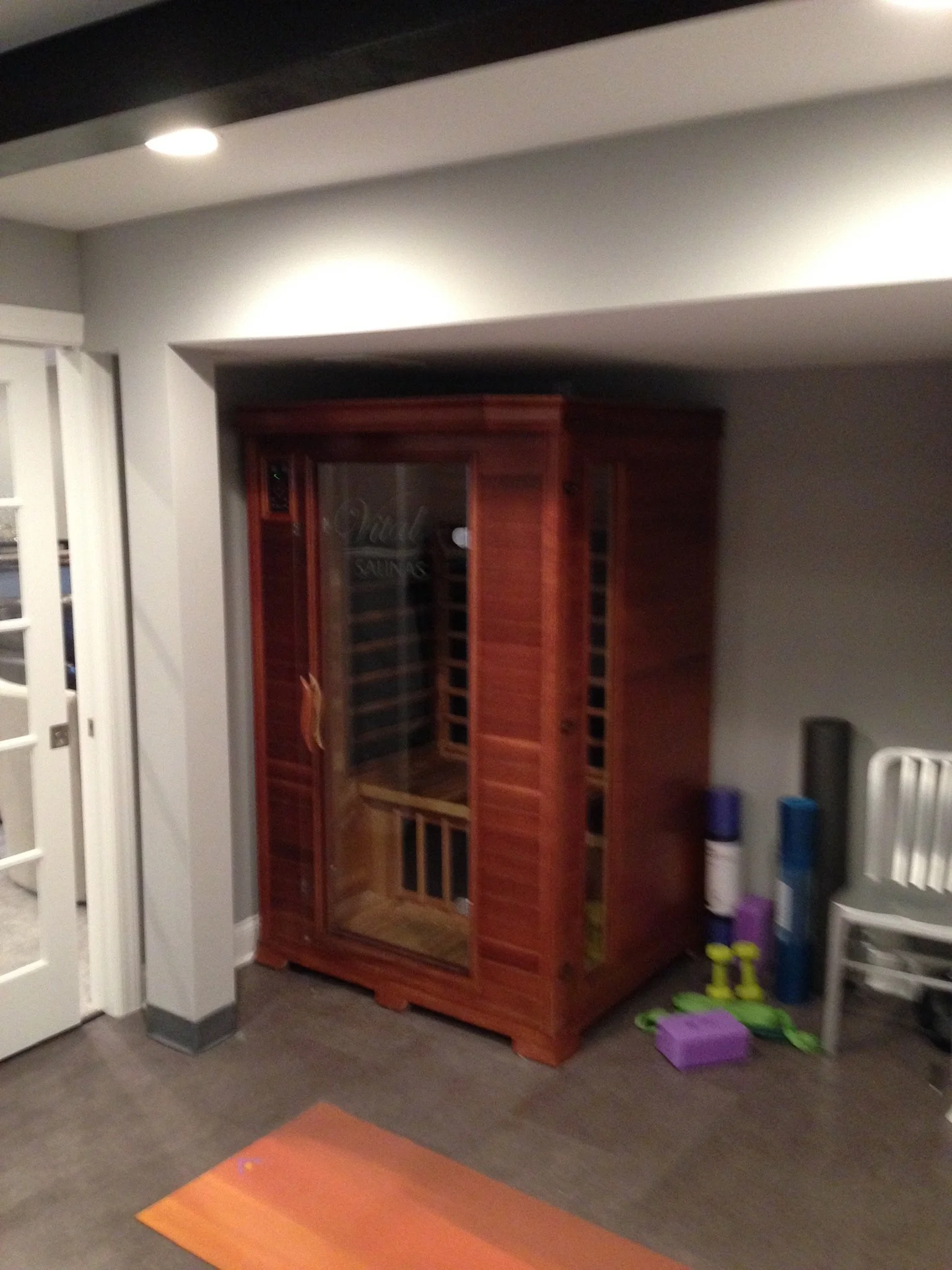 A wooden wine cooler with glass doors in a room corner, with exercise mats and toys nearby.