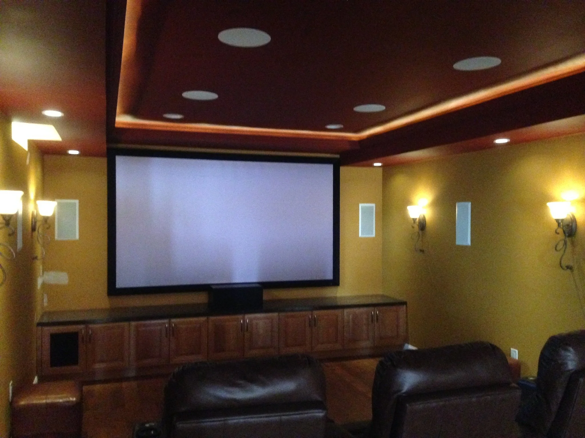 Home theater room with a large projection screen, brown leather chairs, wall-mounted lights, and yellow walls.