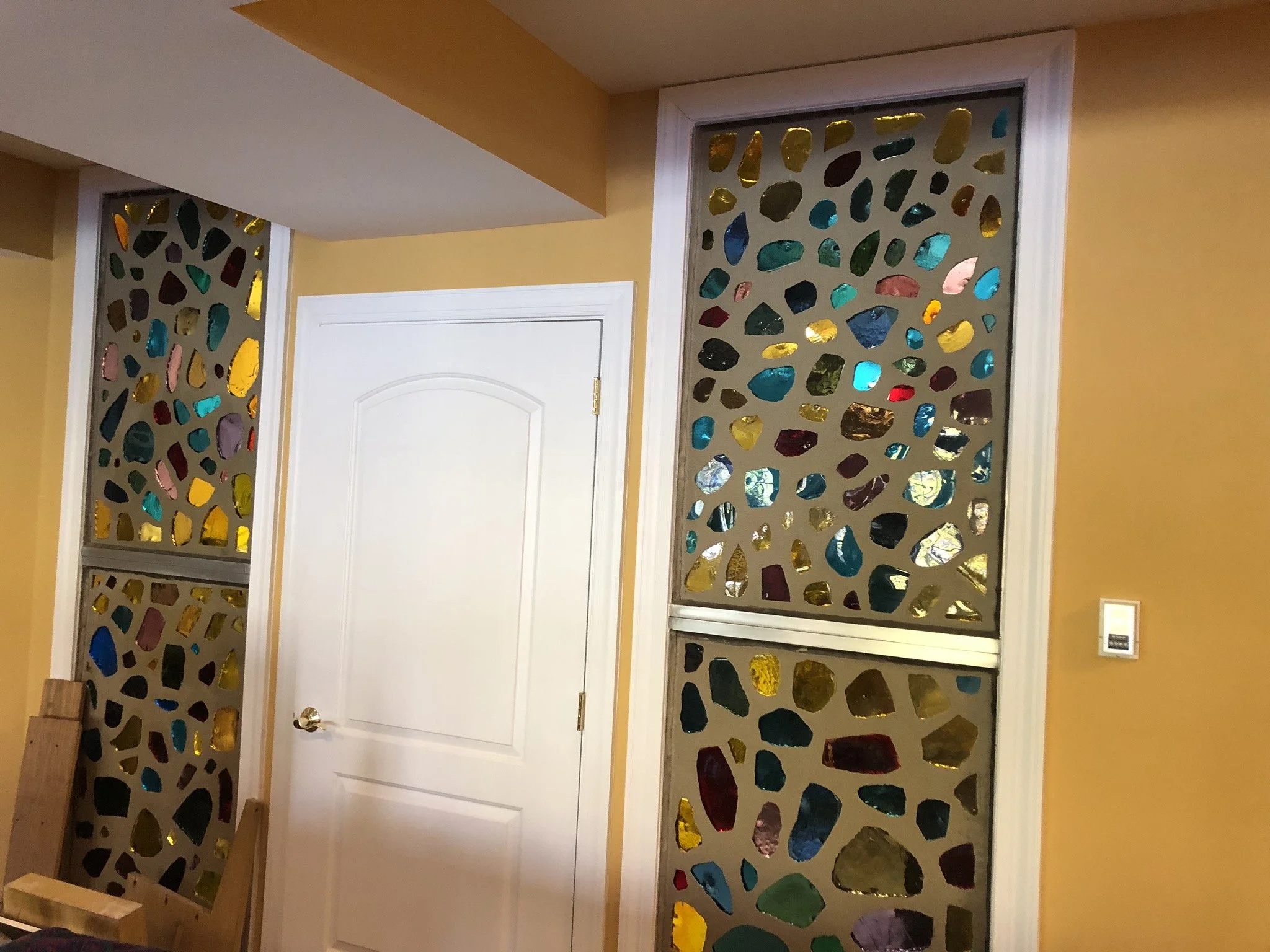 Interior view of a room with a white door and decorative stained glass panels with colorful, irregular glass pieces.