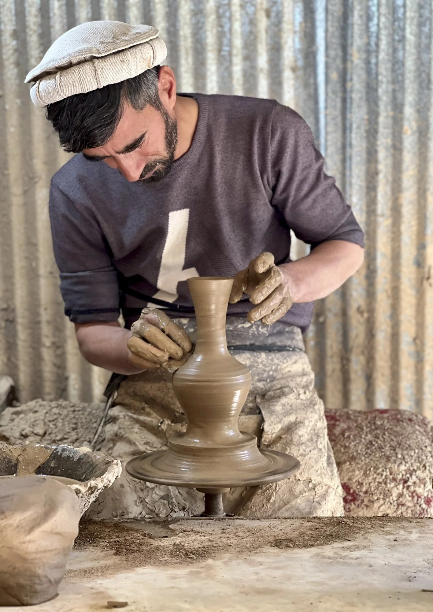 Man shaping a clay vase on a pottery wheel in a ceramics studio
