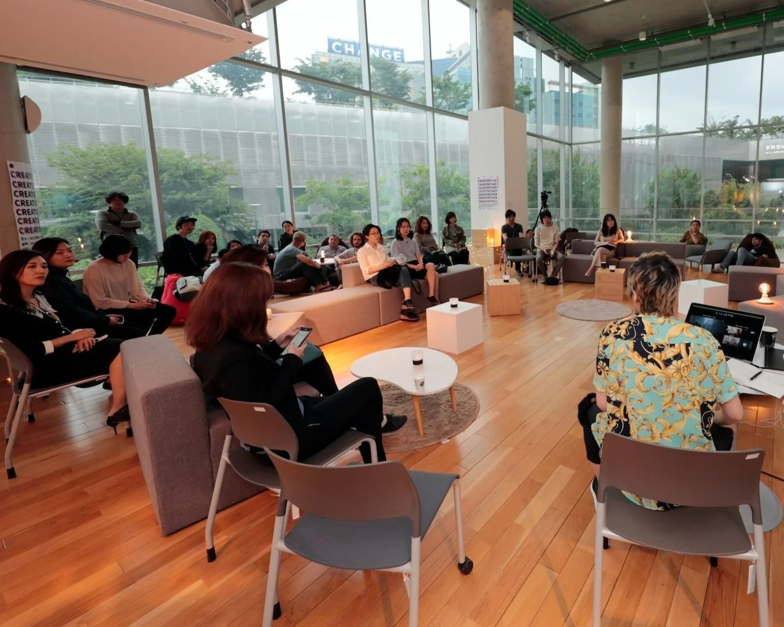 People attending a seminar in a modern room with large windows and wood flooring.