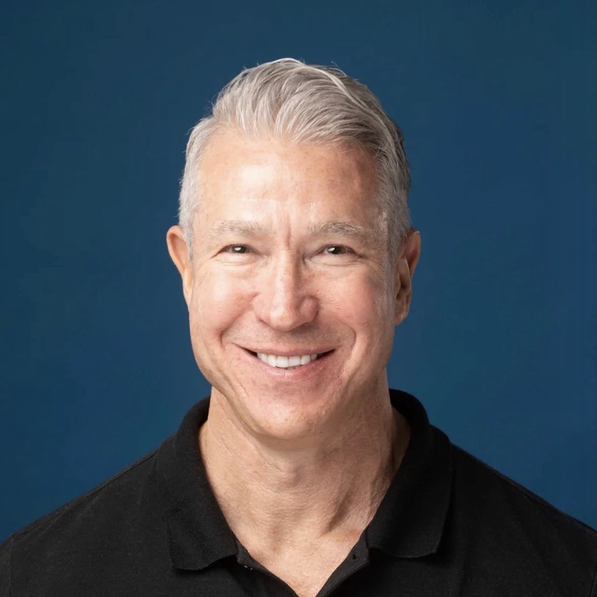 Image of Christopher Laney in a black polo shirt against a blue background.