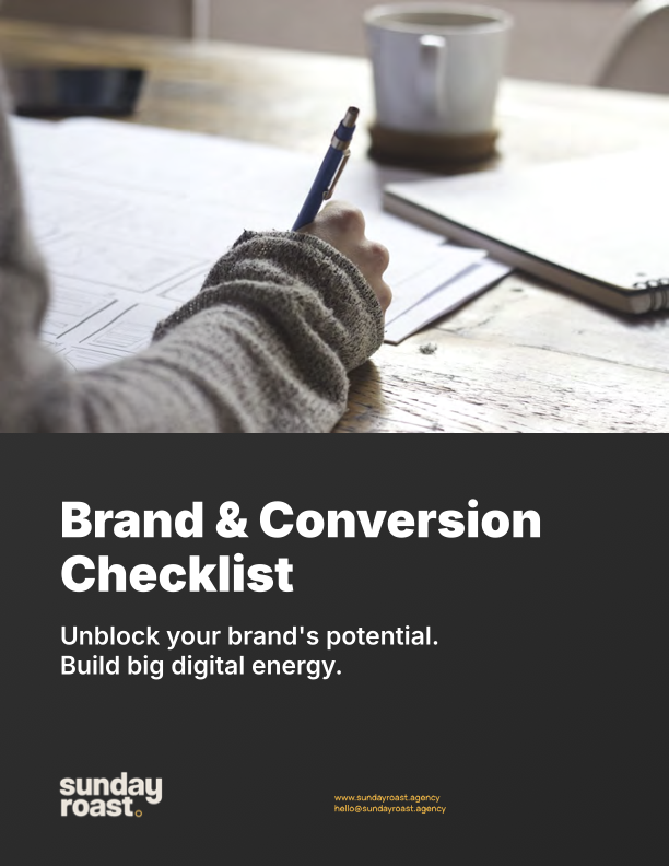 A person writing on paper with a pen at a wooden table, with a coffee mug and a notebook nearby, promoting a Brand & Conversion Checklist by Sunday Roast agency.