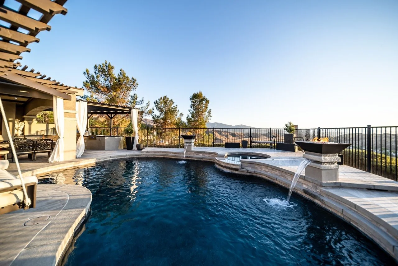 Luxury backyard with a swimming pool, hot tub, shaded seating area, and scenic mountain views under a clear blue sky.