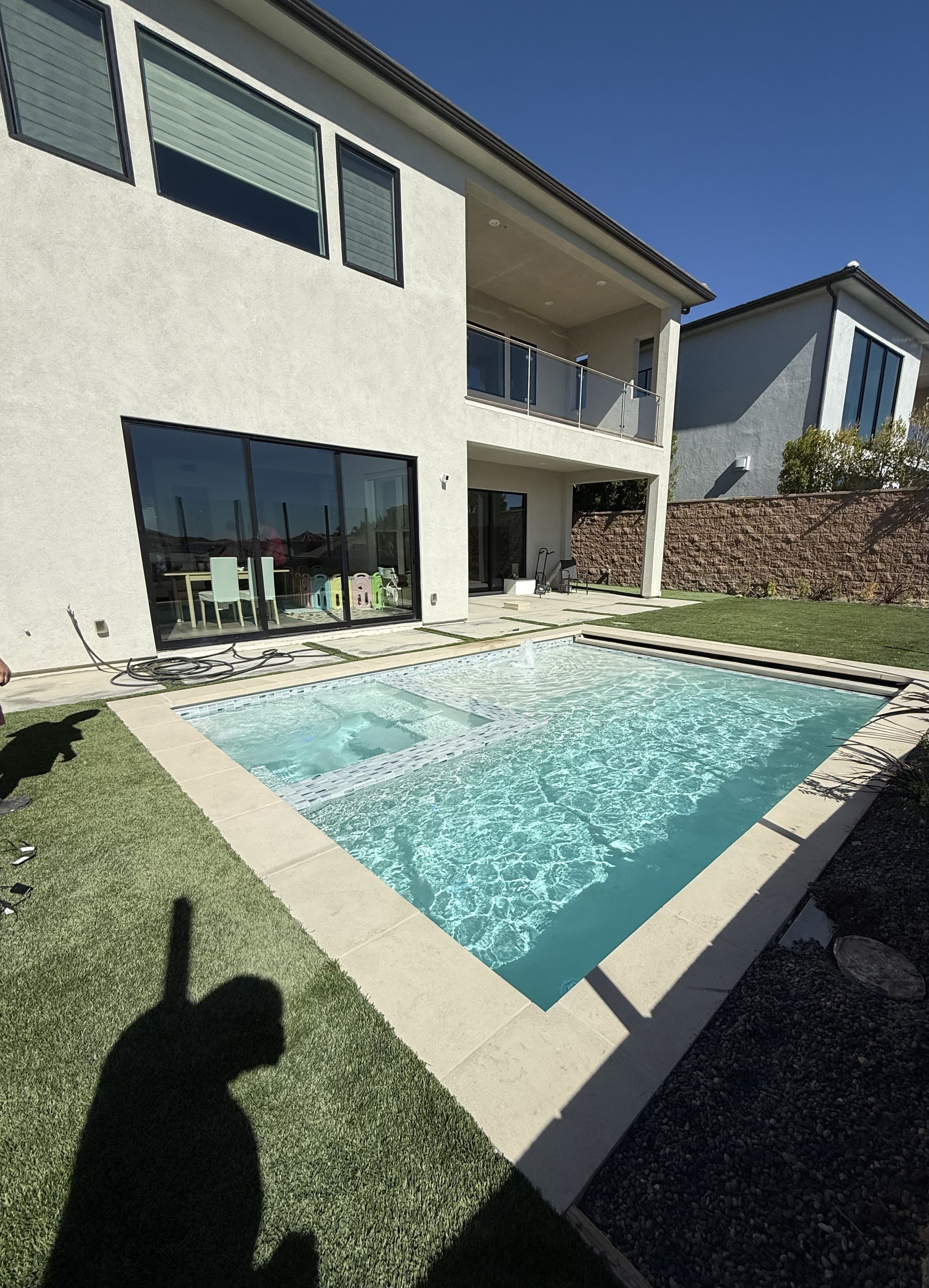 Modern two-story house with a backyard swimming pool, outdoor seating, and landscaped lawn under a clear blue sky.