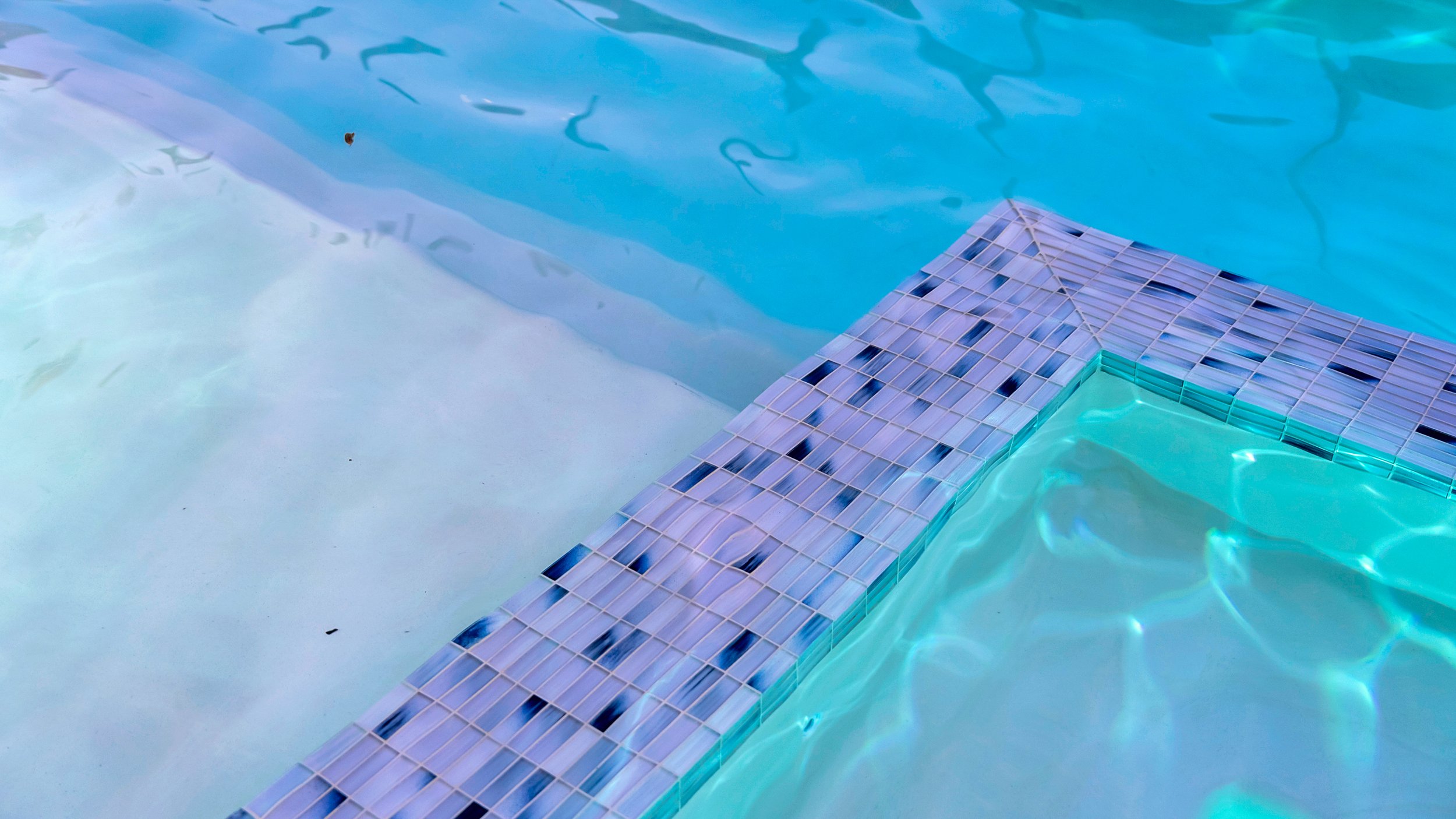 Close-up of a swimming pool with a tiled corner edge and clear blue water.