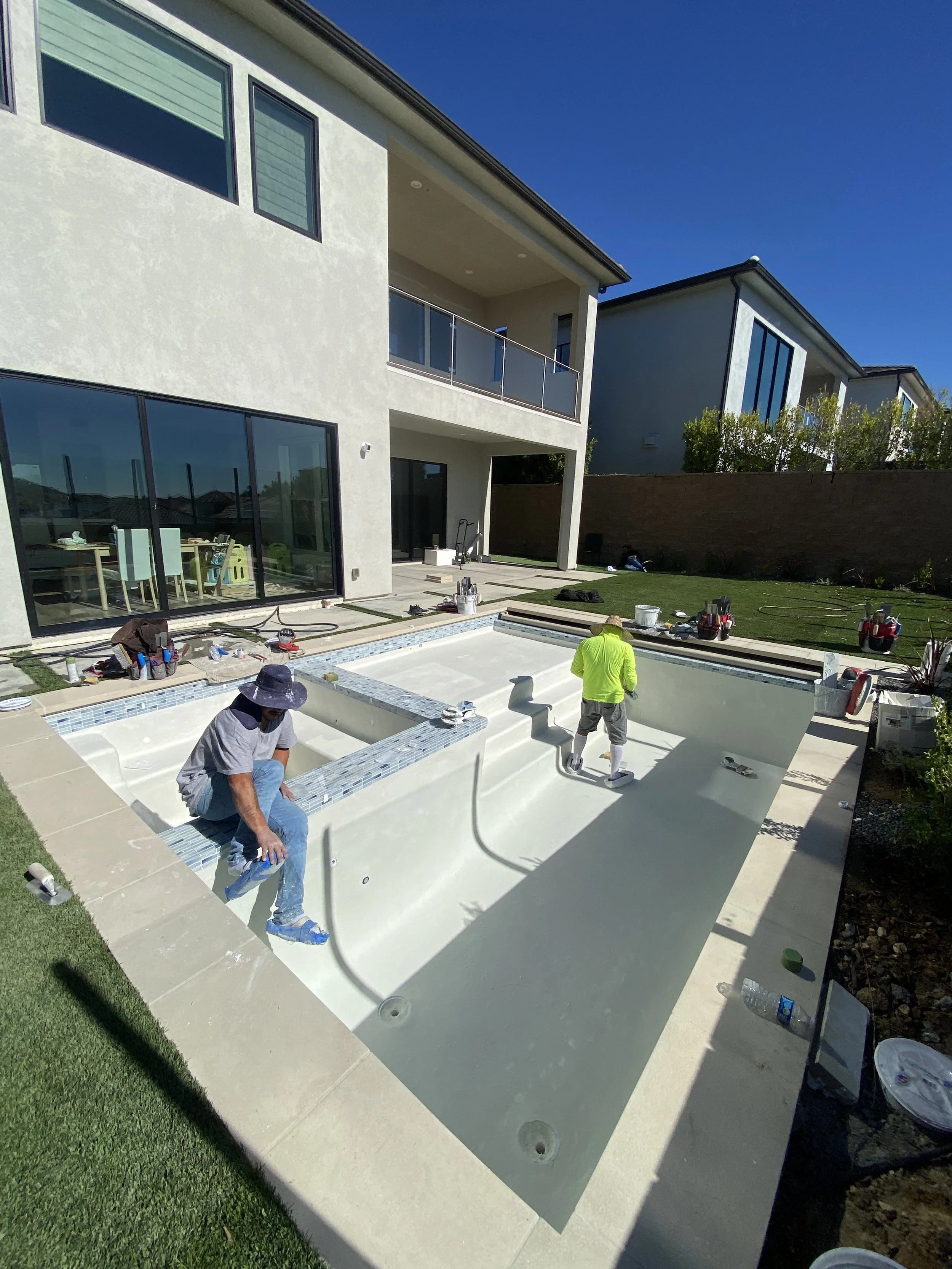 Two construction workers installing a swimming pool in a backyard of a modern house on a sunny day.