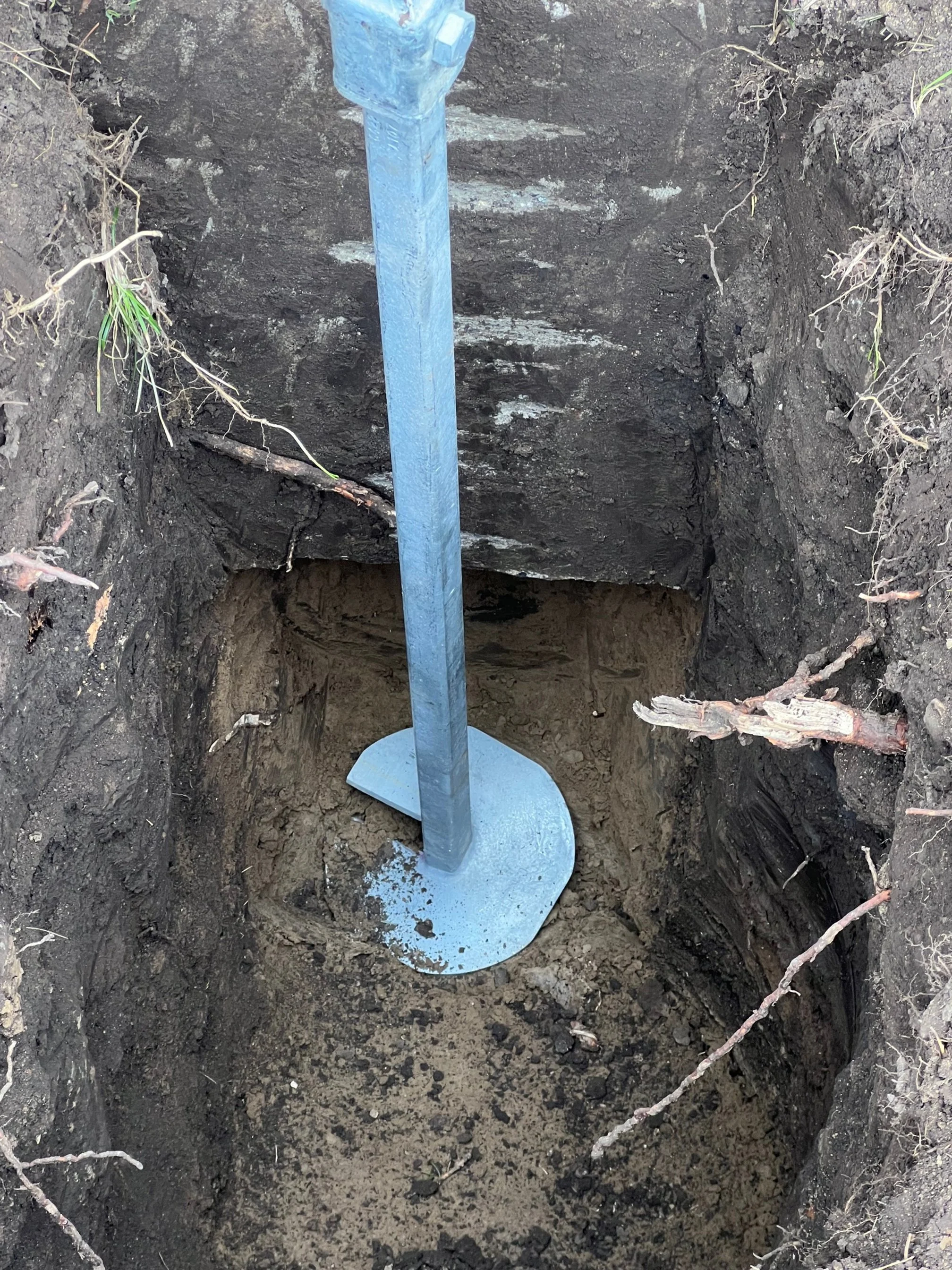 A metal post or stake inserted into the ground inside a deep hole dug into the soil.