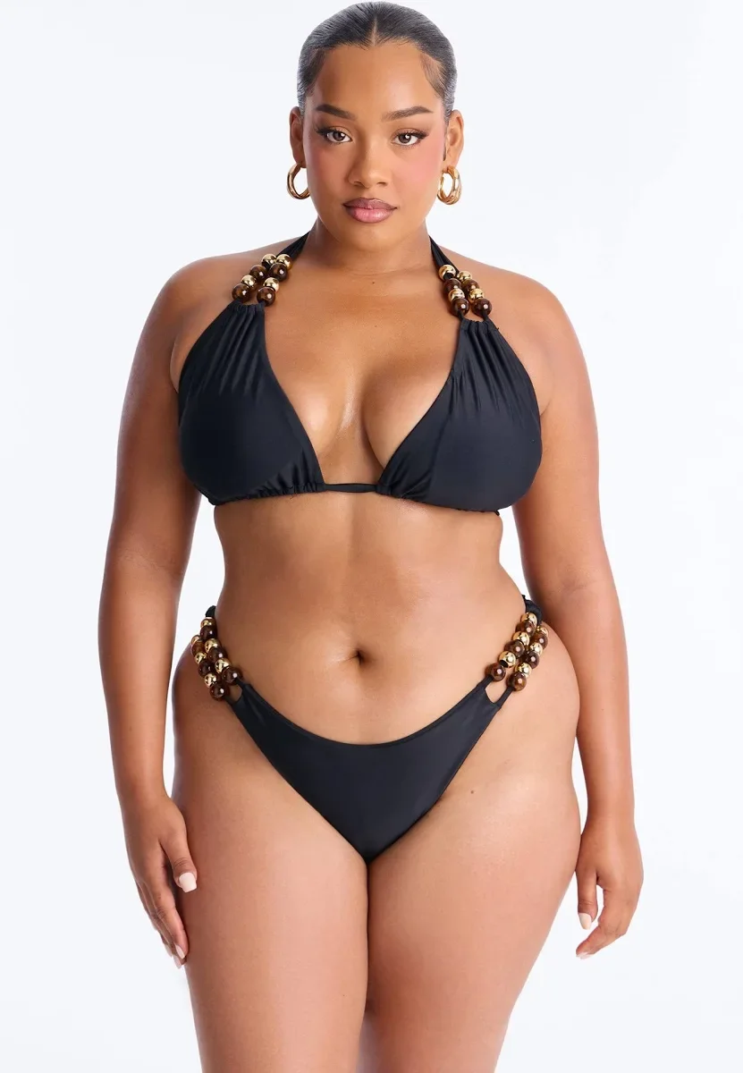 A woman wearing a black bikini with bead detailing on the straps, posing against a plain white background.