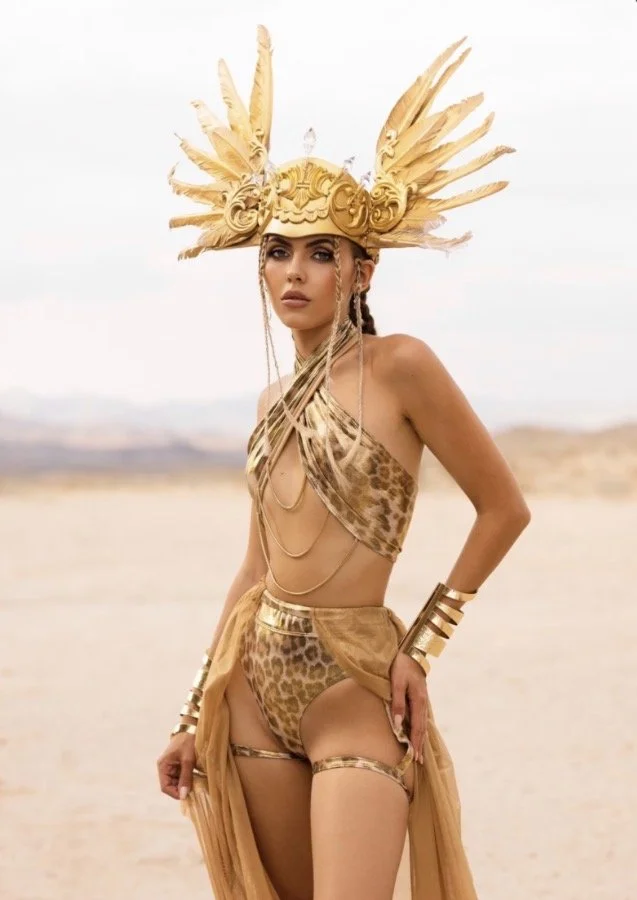 A woman (Modeling) in desert landscape wearing a leopard print outfit with gold accessories and an elaborate gold feathered headdress.