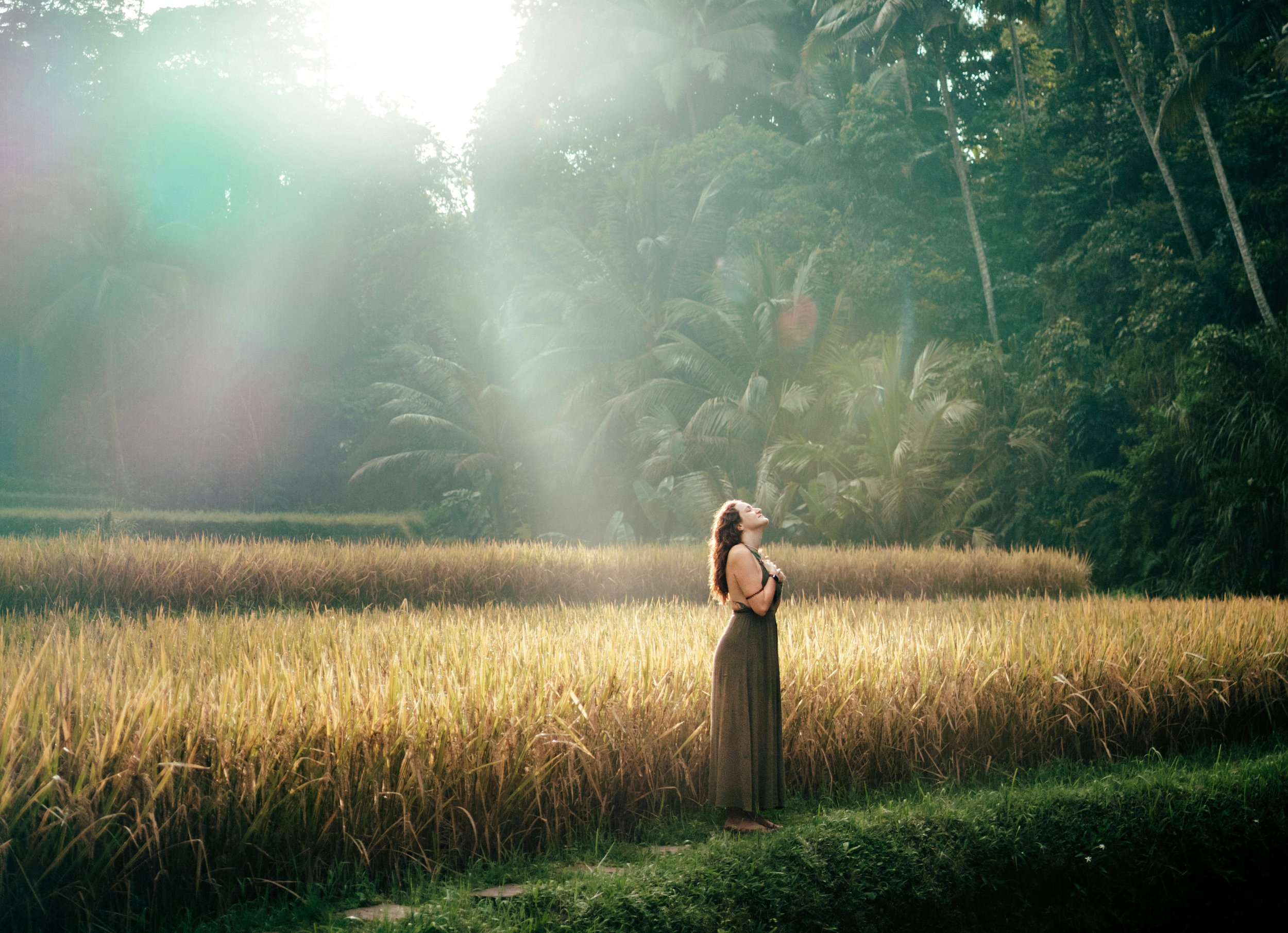 Woman in field with hands on heart and face up as sun rays bless her