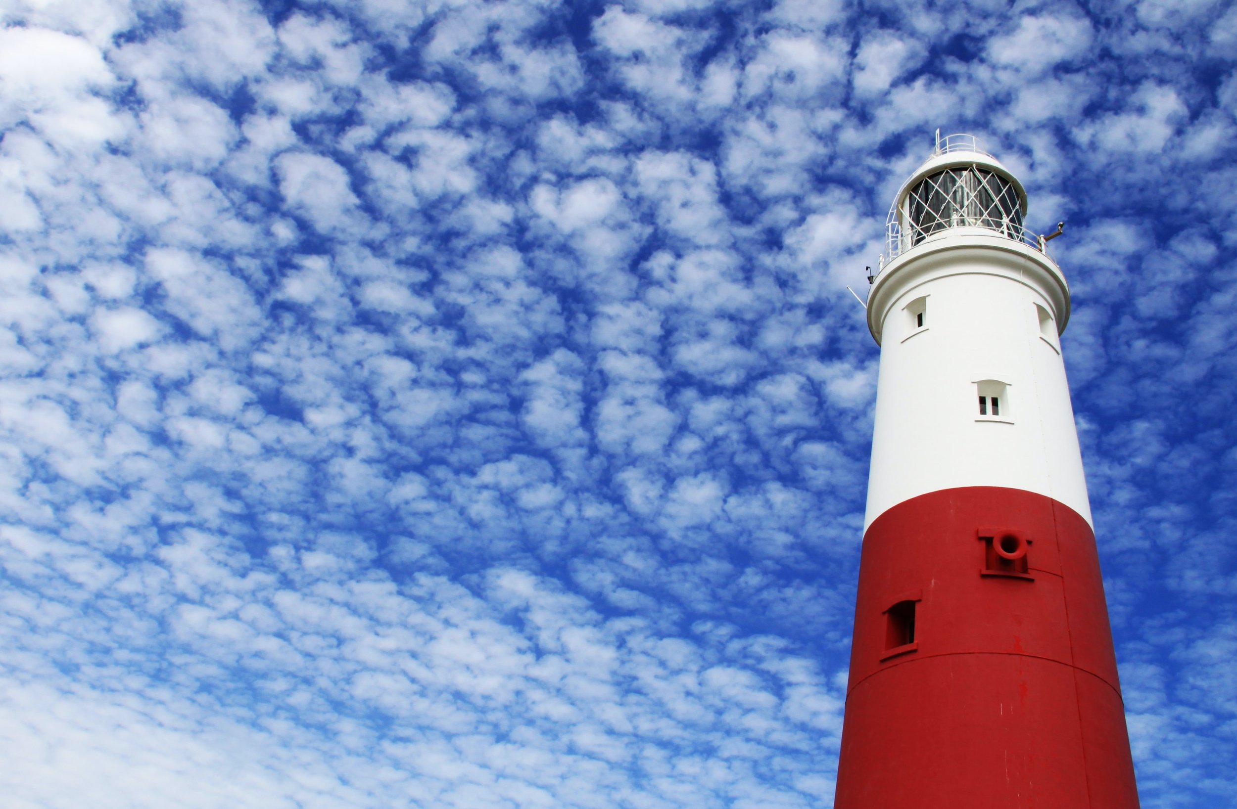 Looking up at a red and white lighthouse and scattered clouds on blue sky