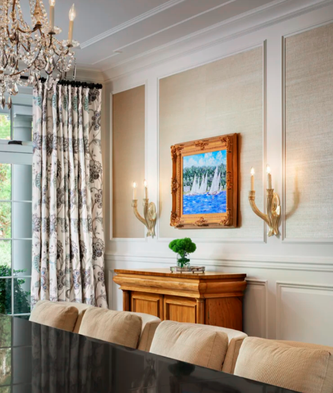 Elegant dining room with a chandelier, patterned curtains, a wooden sideboard, a framed painting of a fountain with water, and a beige upholstered dining bench.