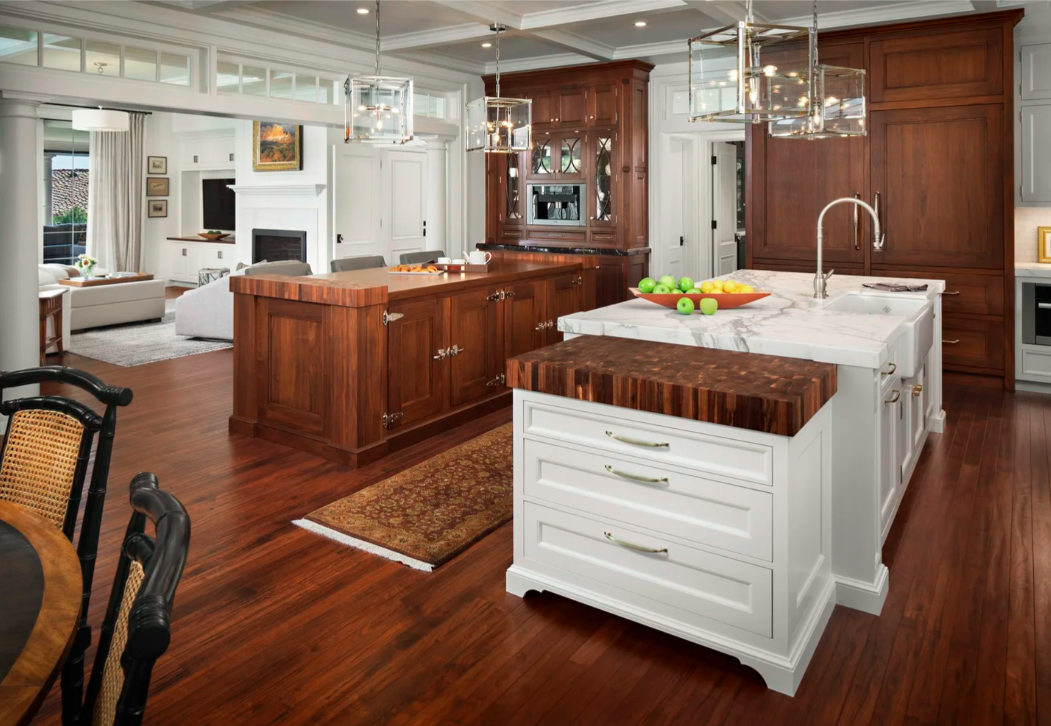 Modern kitchen with white and wooden cabinets, marble island with apples, and pendant lights over the island.