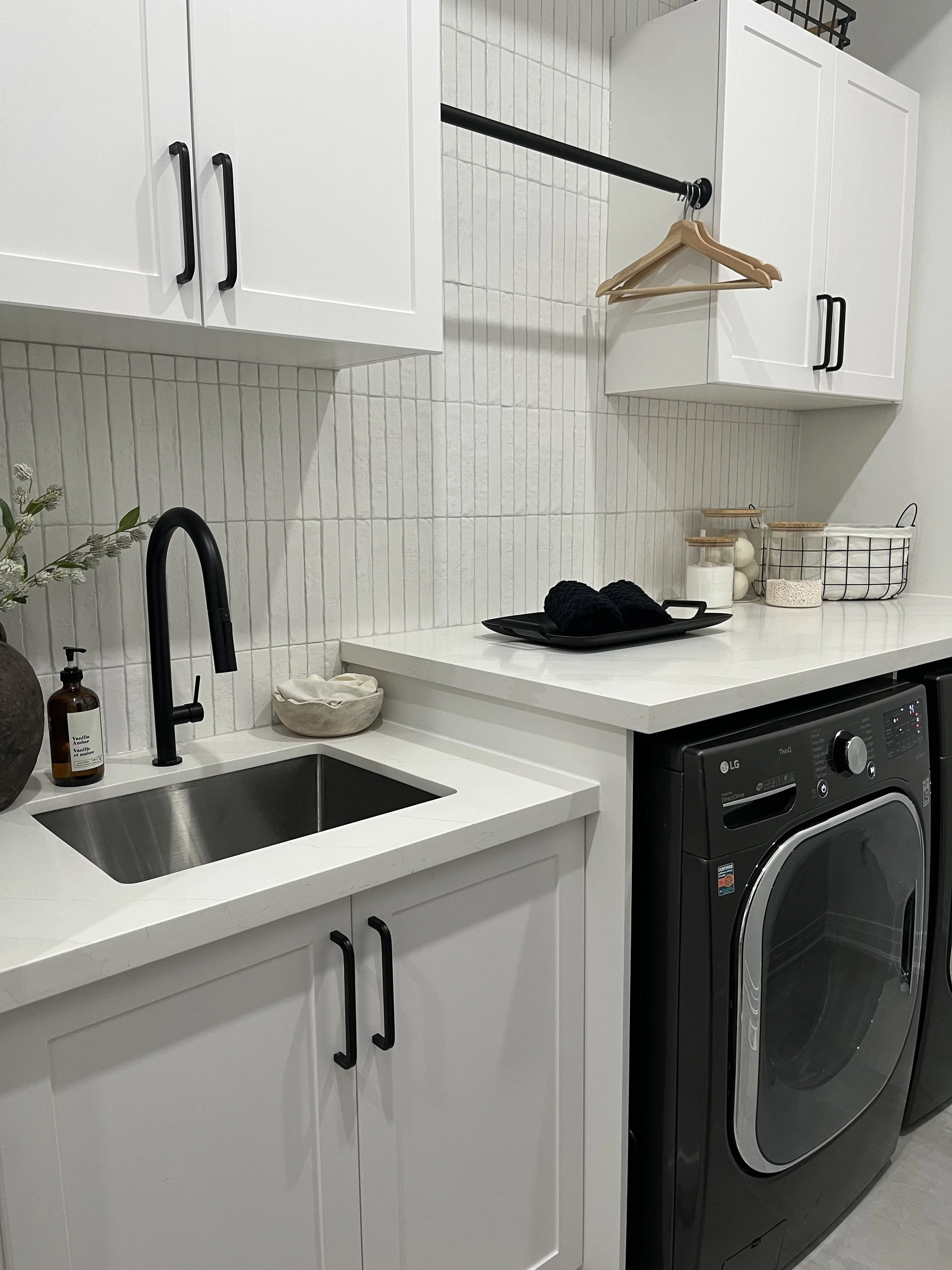 Modern kitchen with white cabinets, black handles, black pendant lights, an island with a black faucet, and stainless steel appliances.
