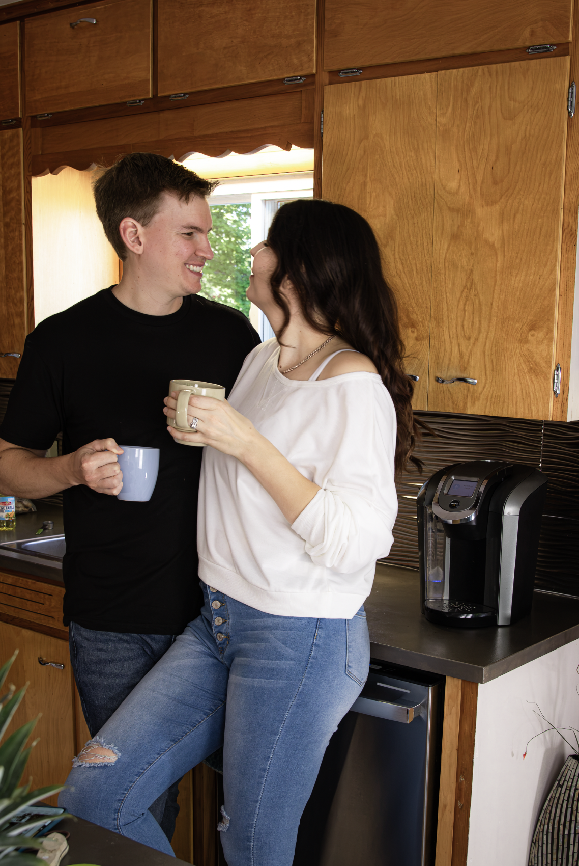 A couple looking at each other while standing in a kitchen and sipping morning coffee.