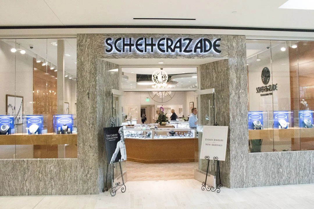 Entrance to Scheherazade jewelry store with sign, display cases and employees inside.