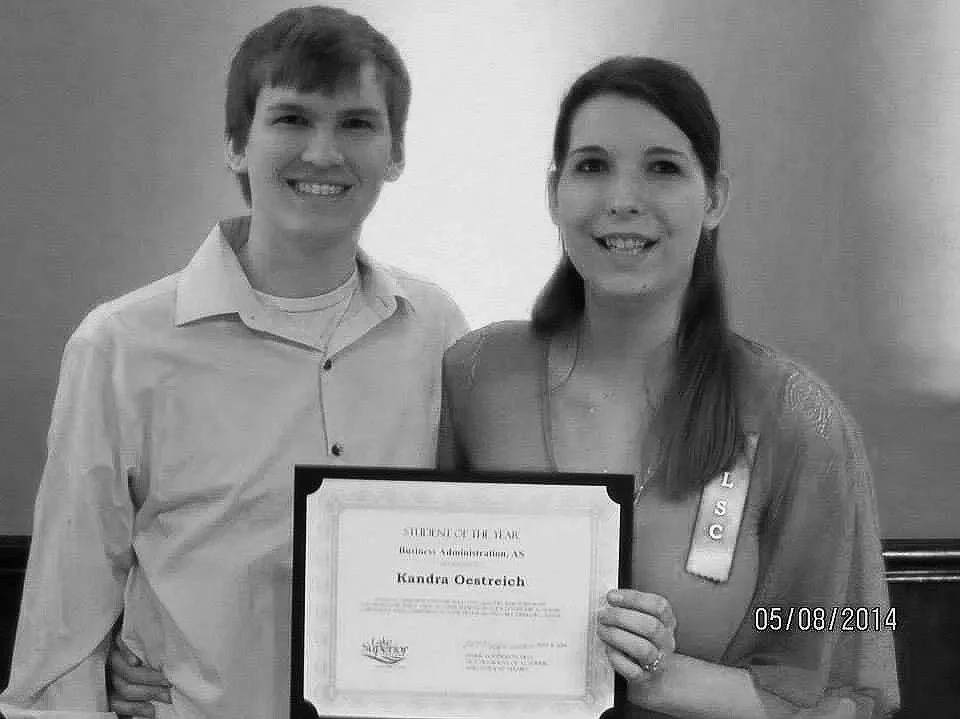A smiling woman holding a certificate of student of the year and standing next to a smiling man in a white shirt.