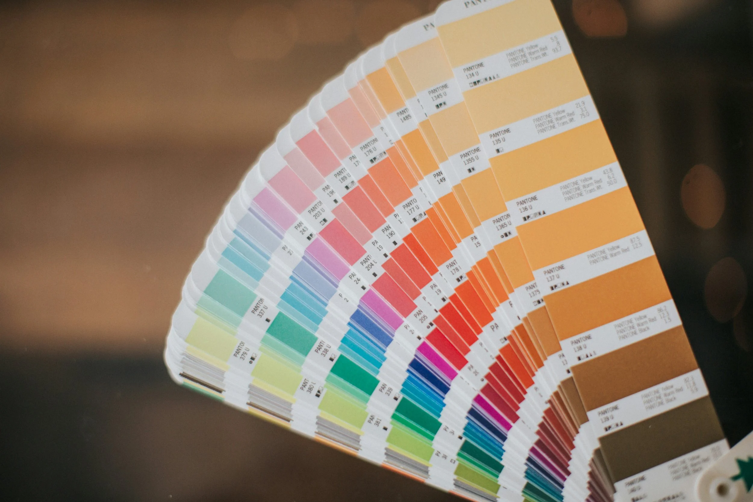 A fan deck of Pantone color swatches arranged in a rainbow gradient, displaying various shades of pink, orange, yellow, green, and blue with specific color codes.