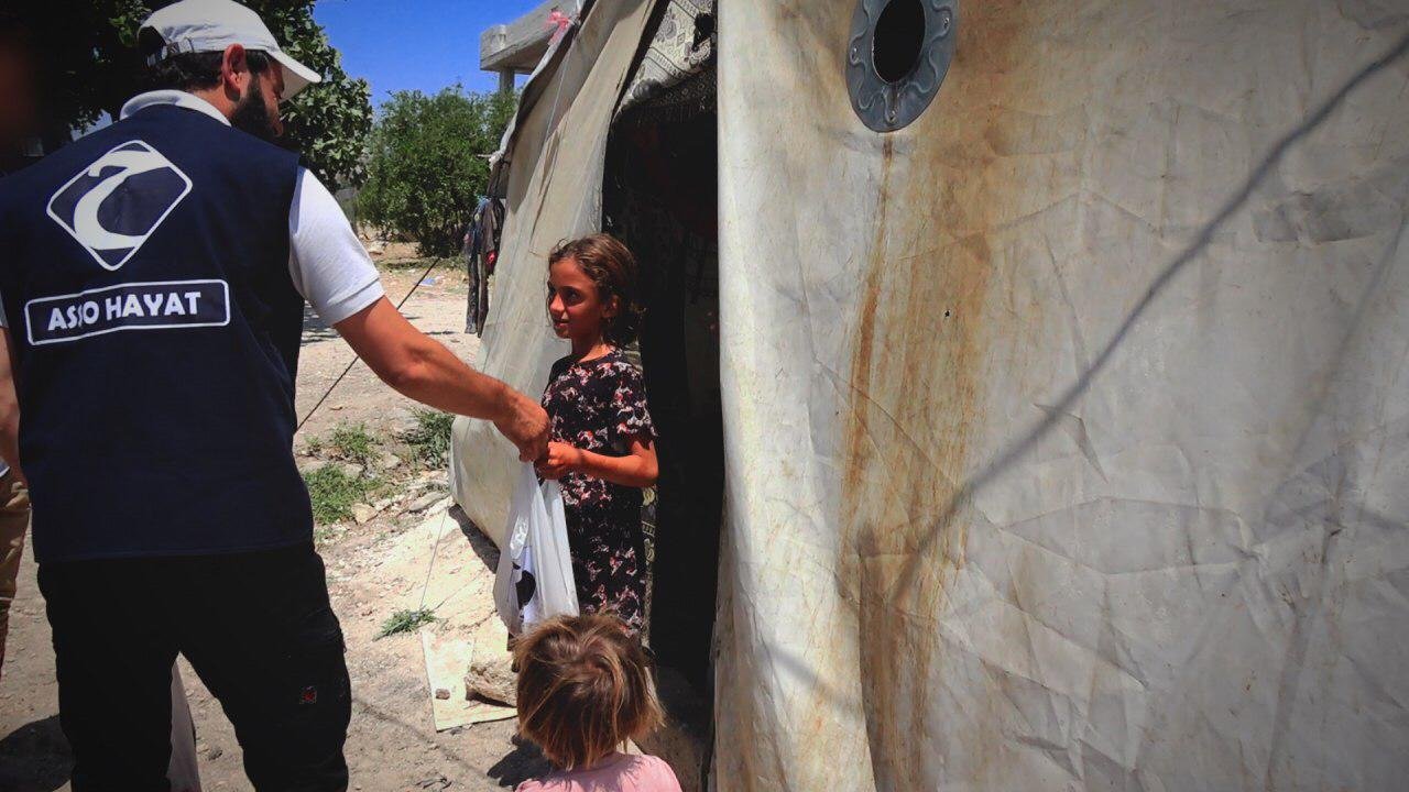 Homme en gilet distribuant un sac à une fille devant une tente.