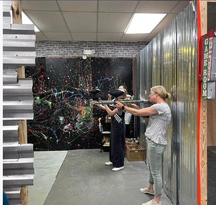 Three people playing laser tag in an indoor game room, with one woman aiming her laser gun at a target.