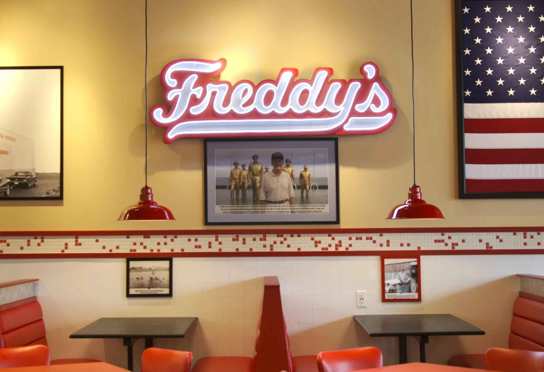 Interior of a Freddy's restaurant with neon Freddy's sign, American flag on the wall, framed photos, and red booths.