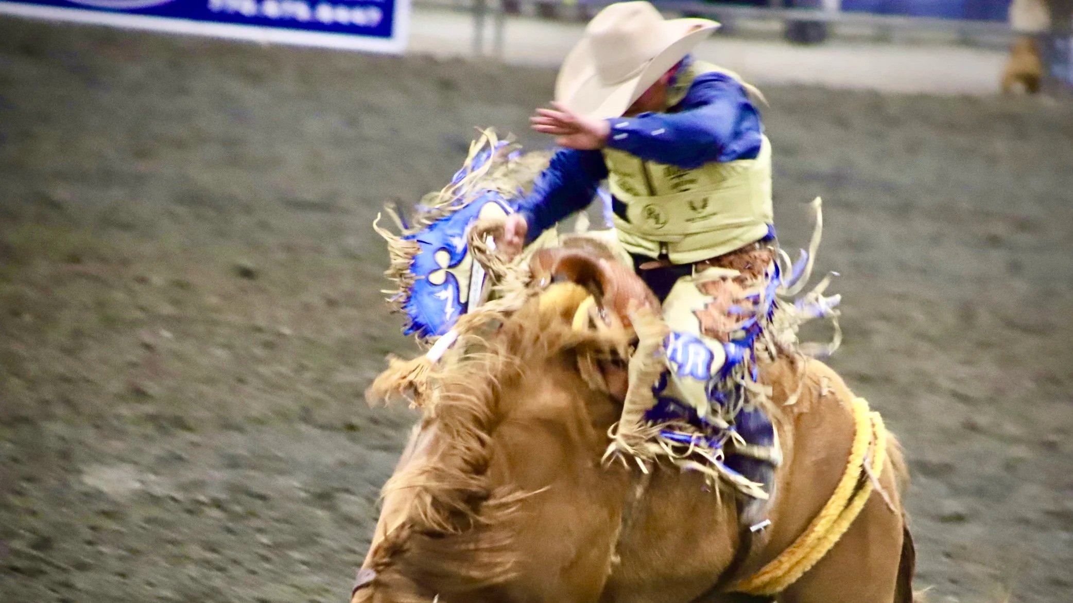 A cowboy riding a bucking horse in a rodeo arena.