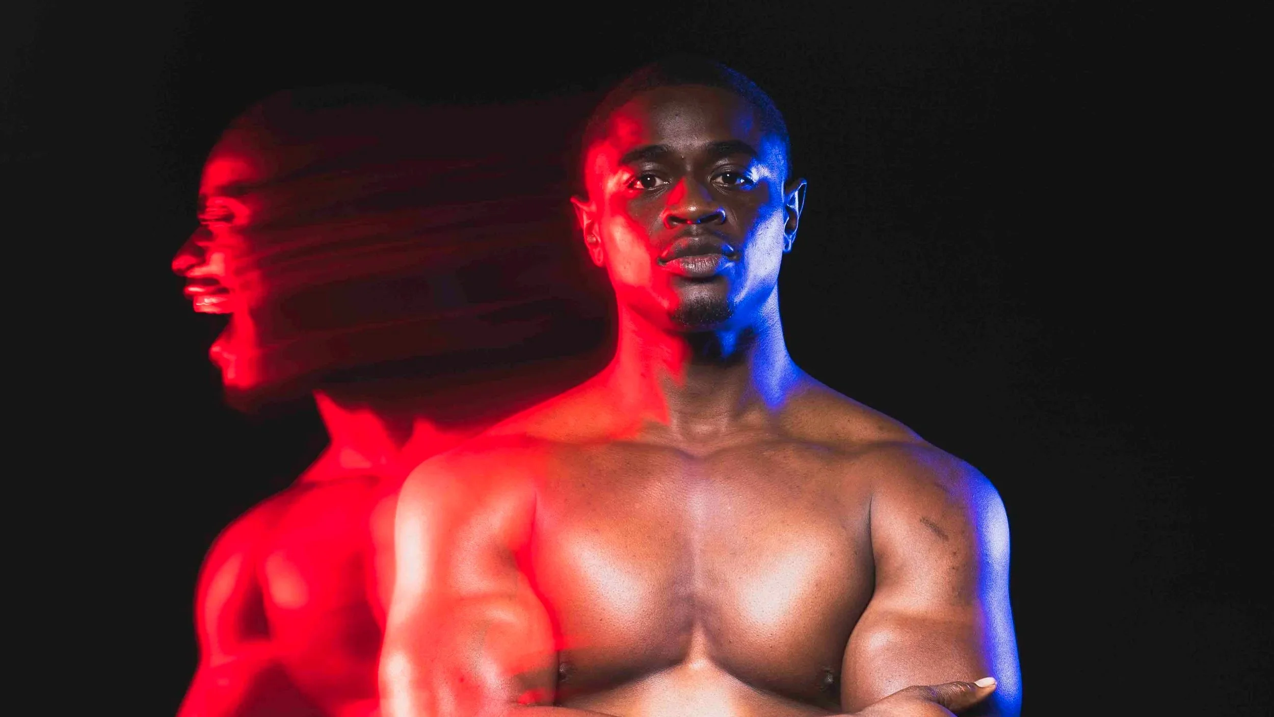 A shirtless Black man with short hair looks directly at the camera against a black background. Neon red and blue lighting highlight his face and upper body, with a motion blur effect creating multiple overlapping images on the left side of his face.