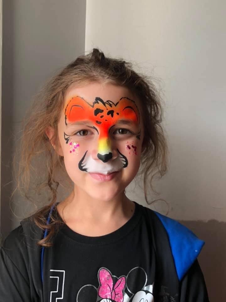 Child with face paint of a fox, wearing a black shirt with a Minnie Mouse graphic, smiling.