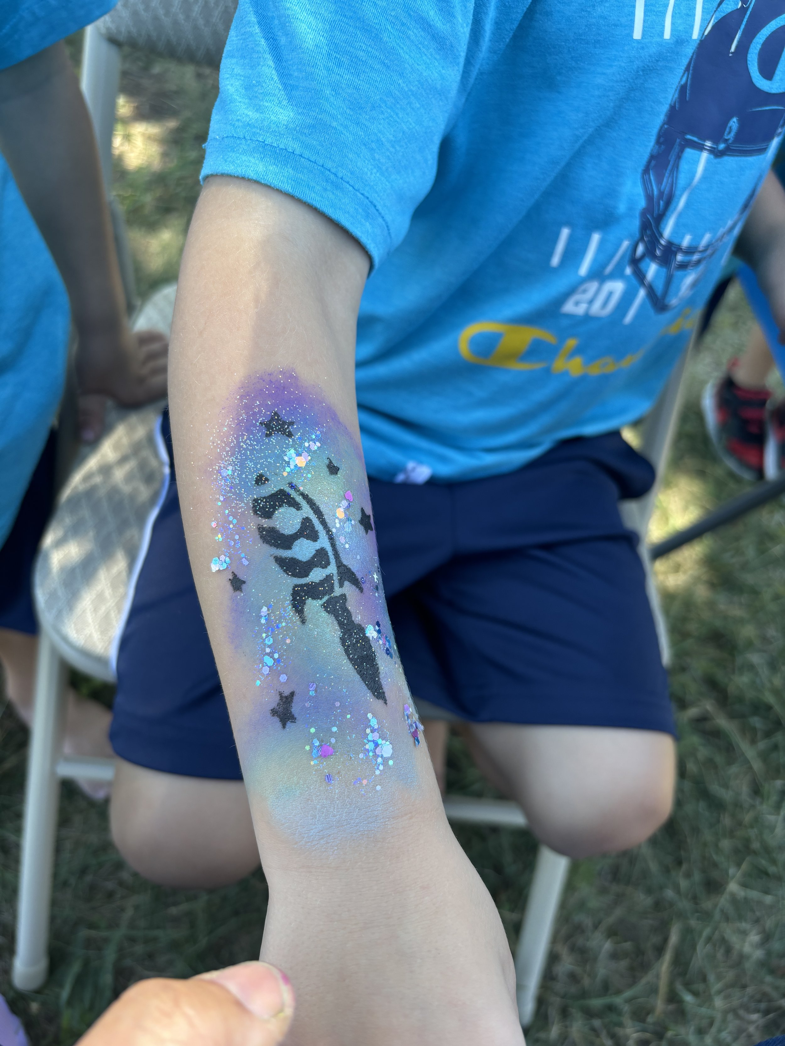 Child with glittery rainbow unicorn temporary tattoo on arm and stars, outdoors on a sunny day.