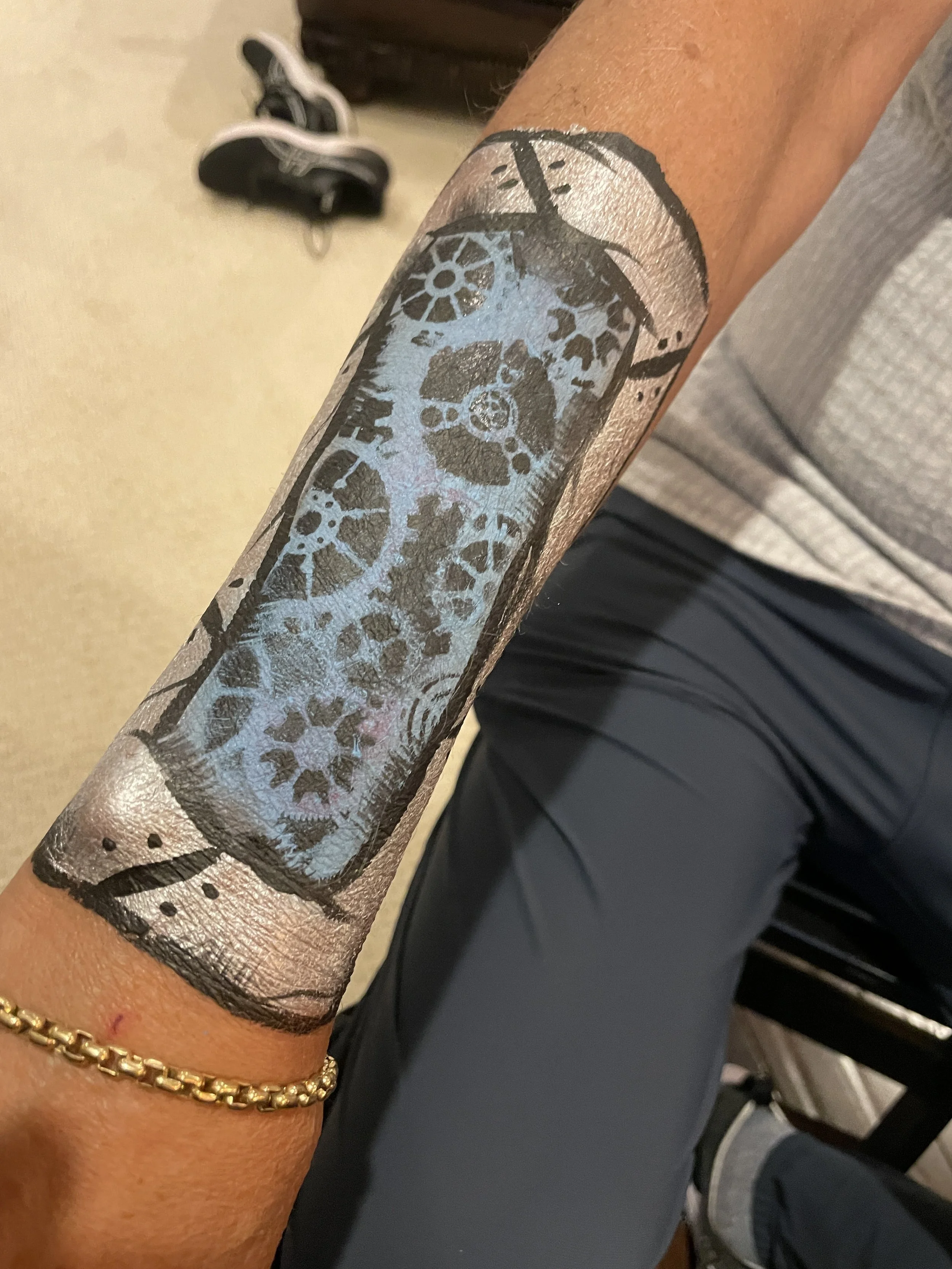 Tattoo of a smartphone with a gear and clockwork design on a person's forearm.