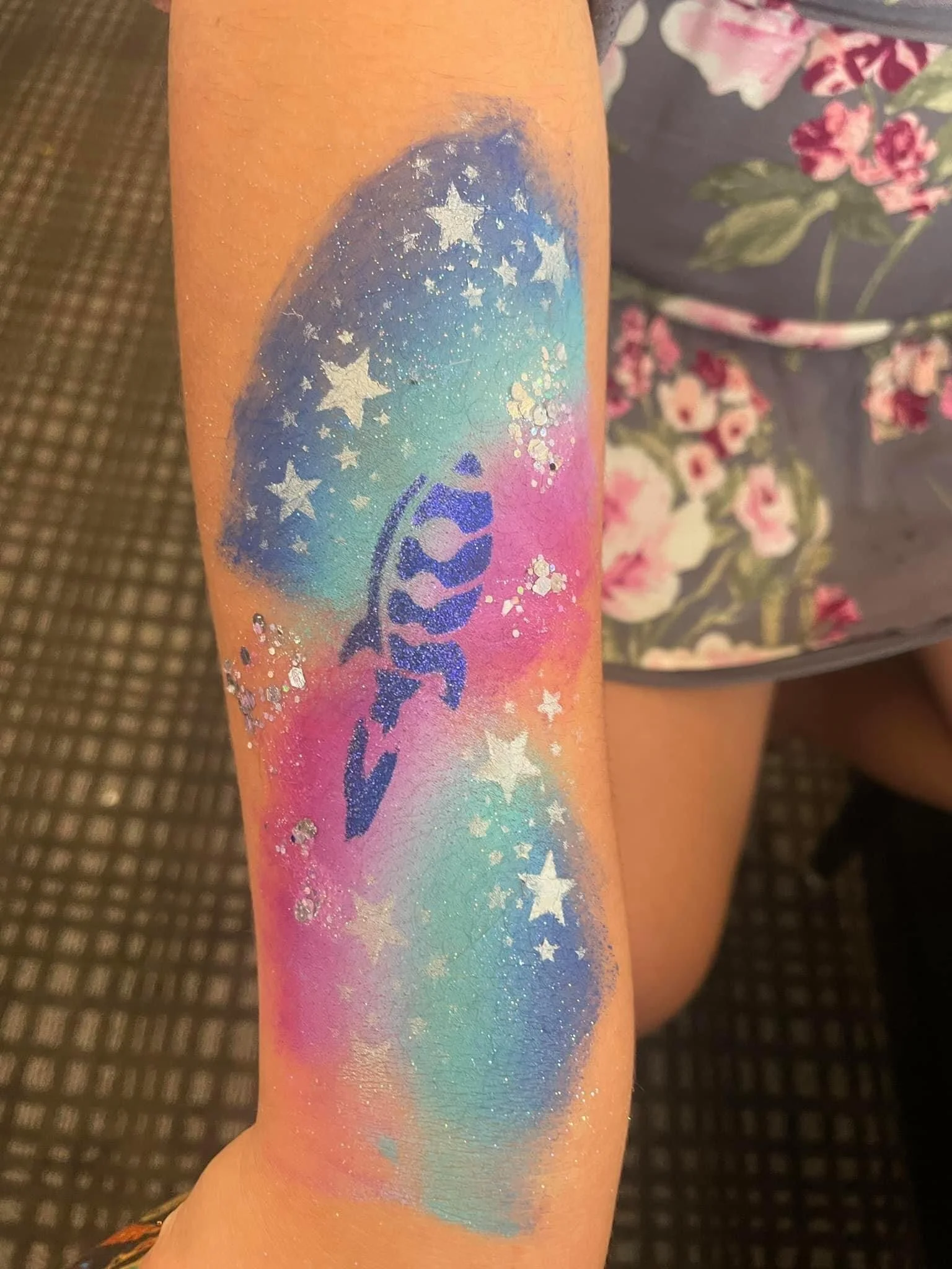 Colorful galaxy tattoo design featuring stars, a fish, and rainbow hues on a person's arm.