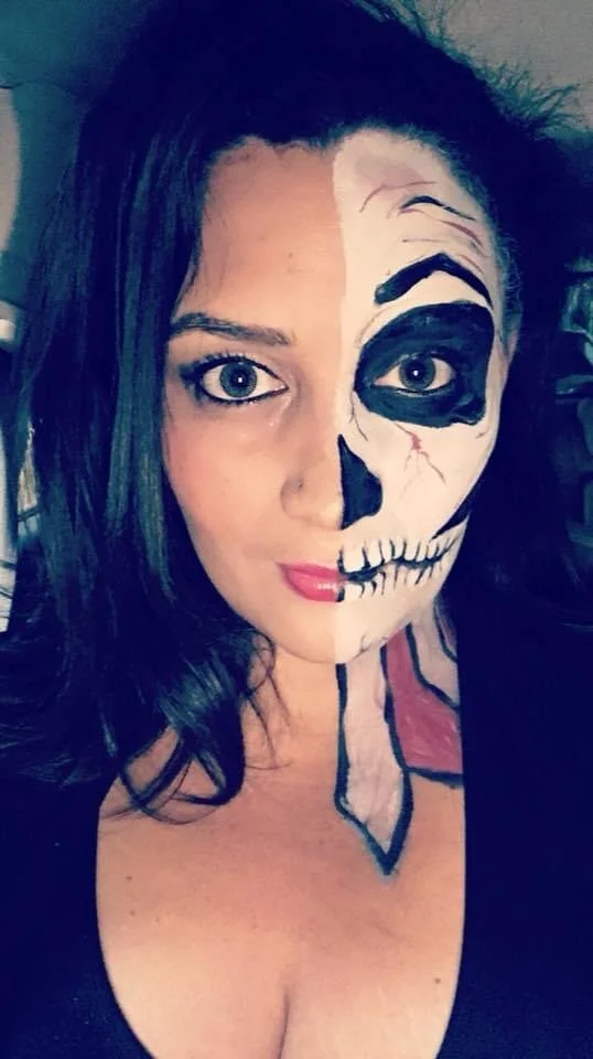A woman with half face painted as a skull and the other half natural, black hair, and blue eyes.