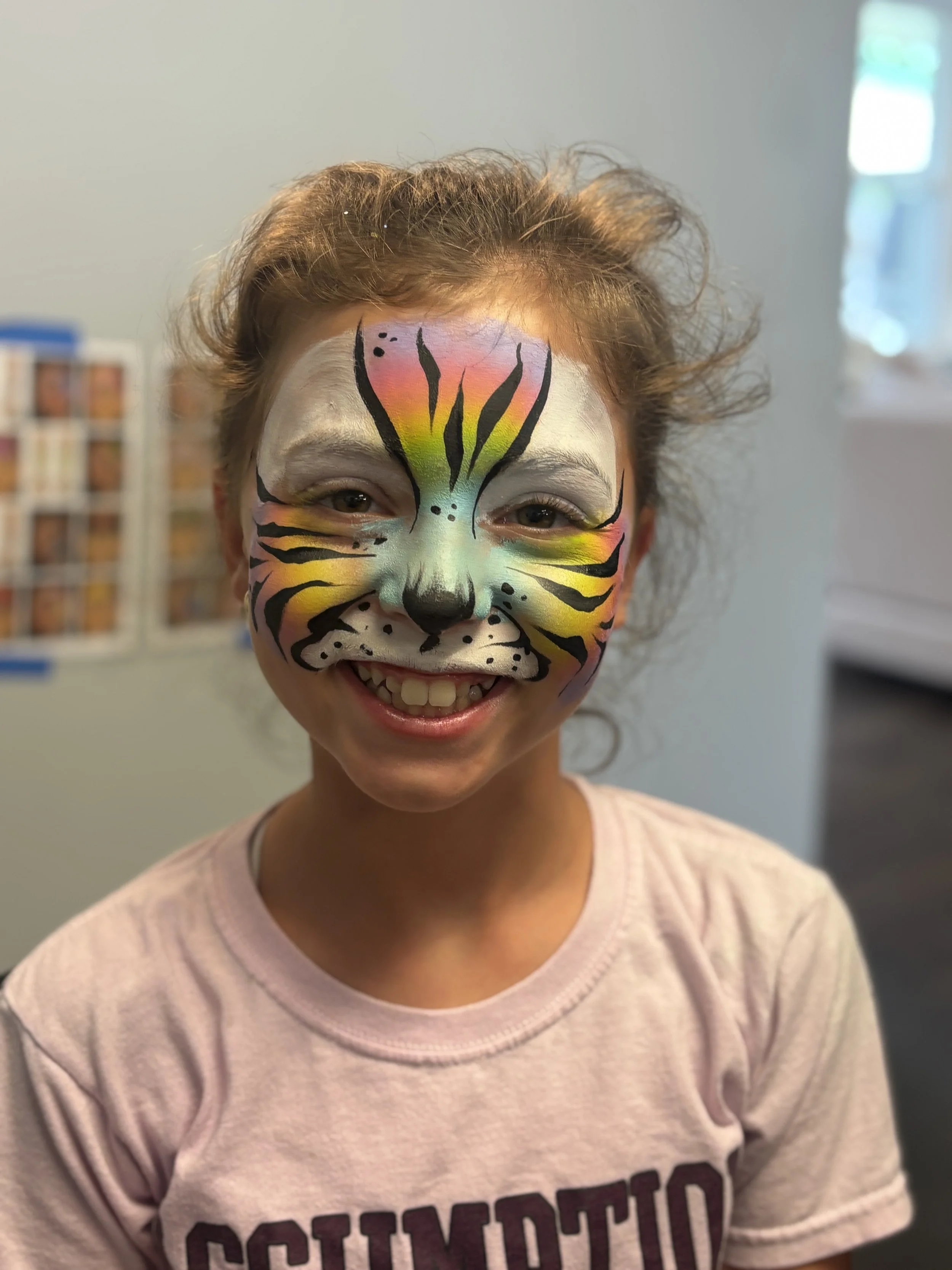 A young girl with a colorful tiger face paint, smiling.