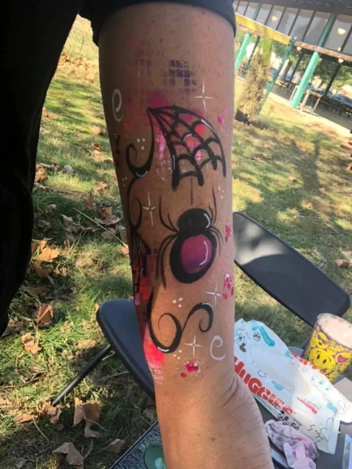 Tattoo of a cartoonish dog with a pink nose, surrounded by the word 'love' and decorative elements on a person's forearm outdoors.