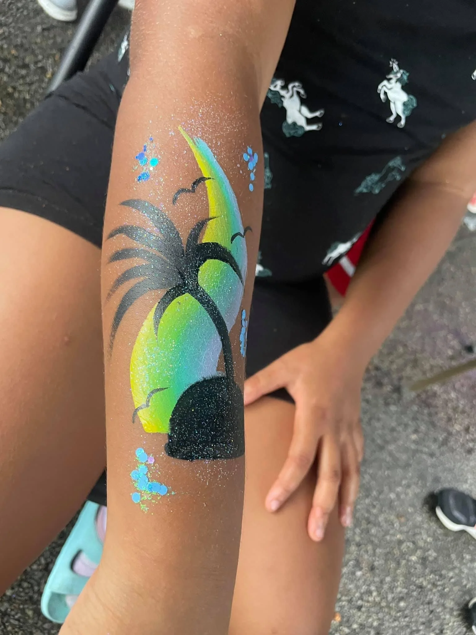 Colorful temporary tattoo of a beach scene with a palm tree, sun, and birds on a person's arm.