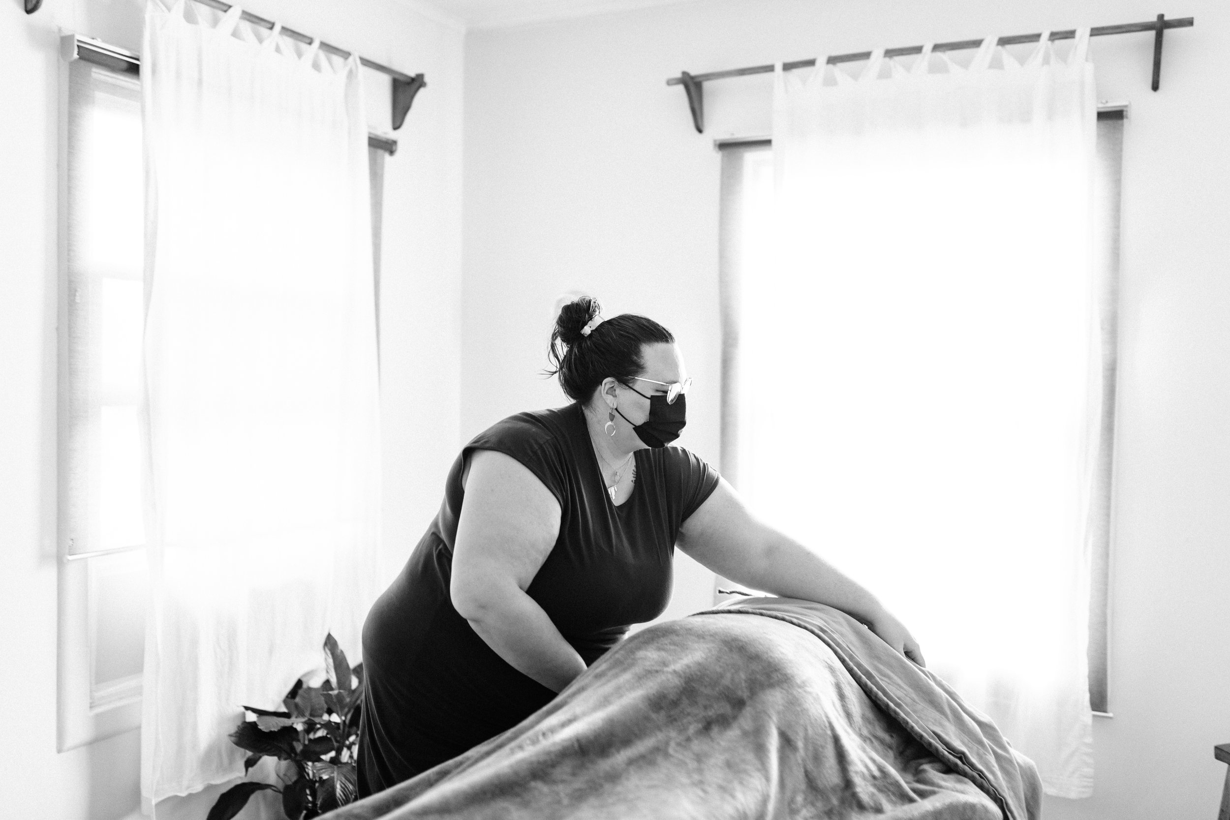 Massage therapist wearing a mask working on a client on a massage table in a sunlit room.