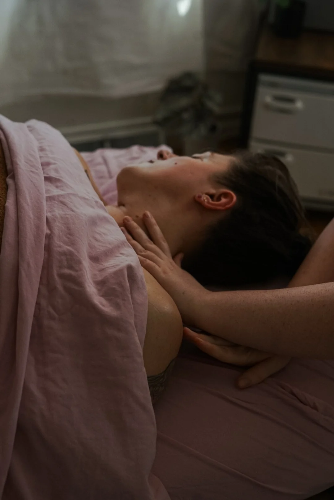 Person lying on bed, receiving a neck massage from another person